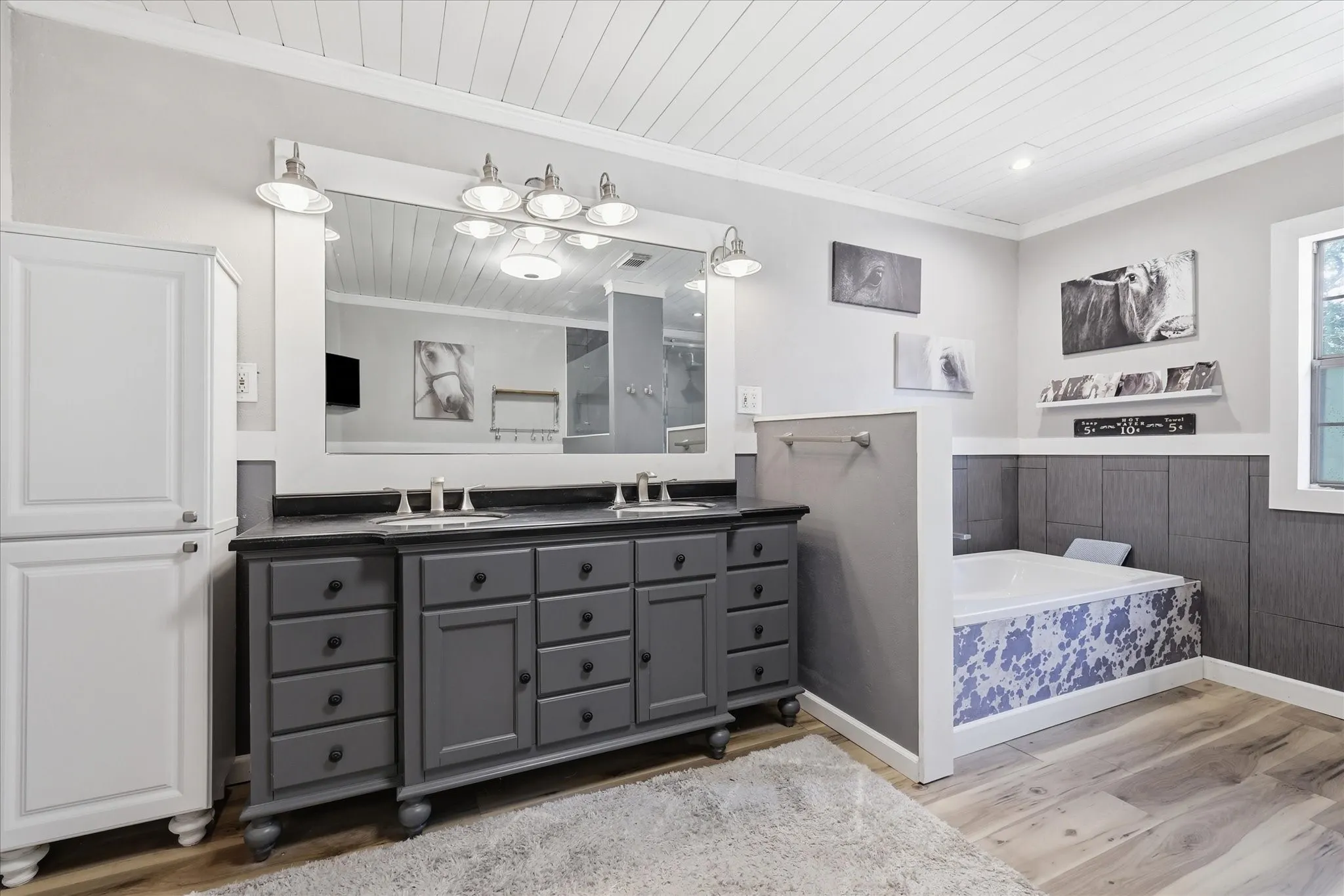 Dual sink vanity with dark cabinetry, integrated countertop, and an expansive wall-mounted mirror