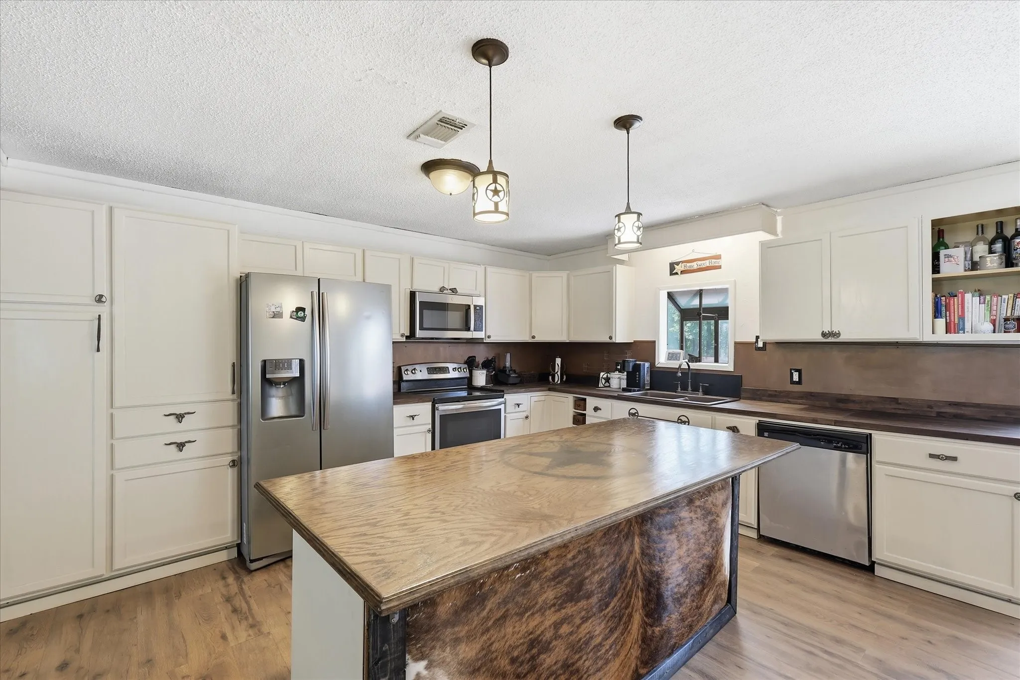 Kitchen featuring an expansive center island with a wood-finish countertop, wood-finish flooring, white cabinetry, stainless steel appliances, and a double basin sink
