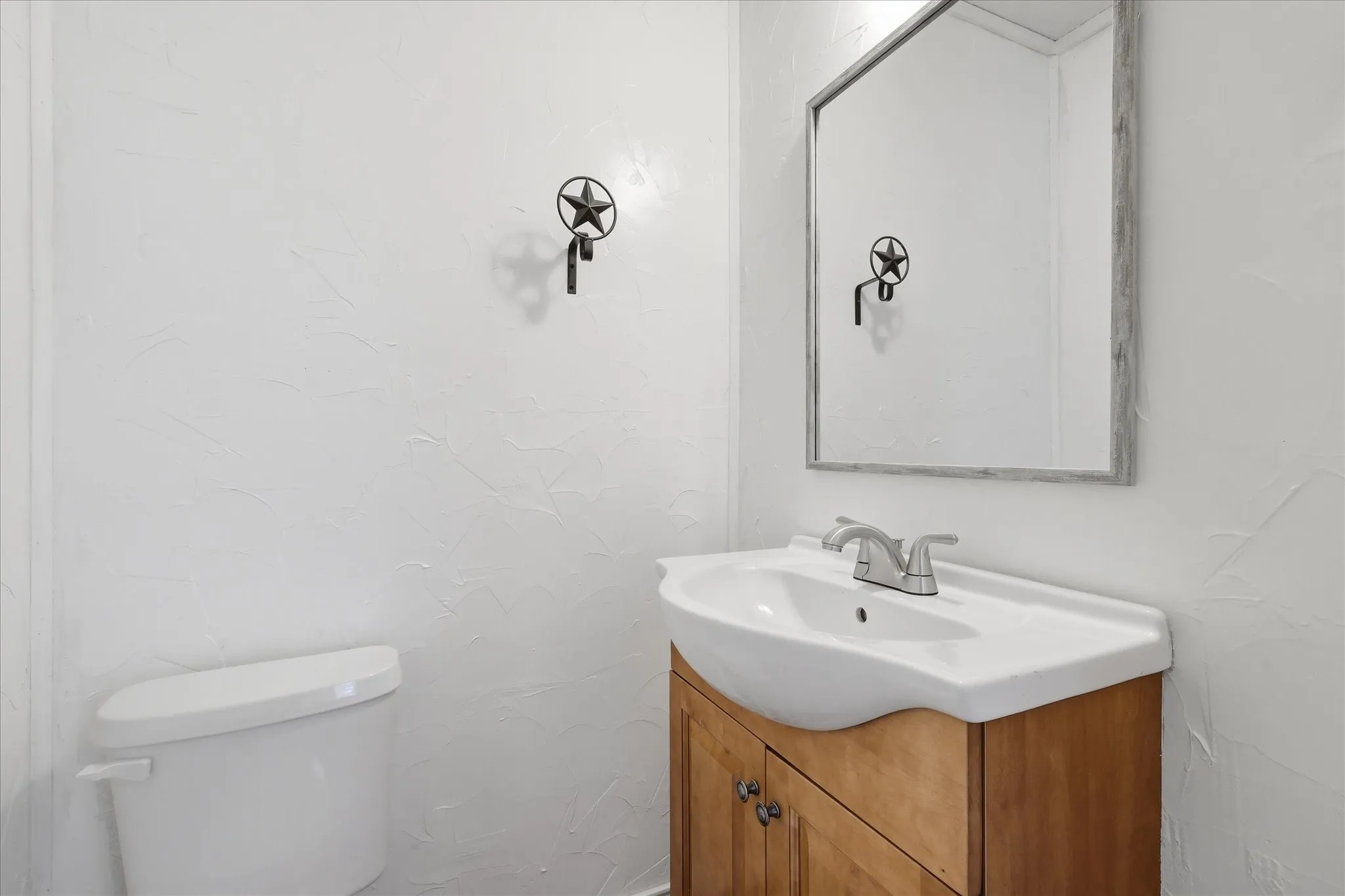 Bathroom vanity featuring a light wood-finish cabinet, white ceramic sink, and a framed mirror