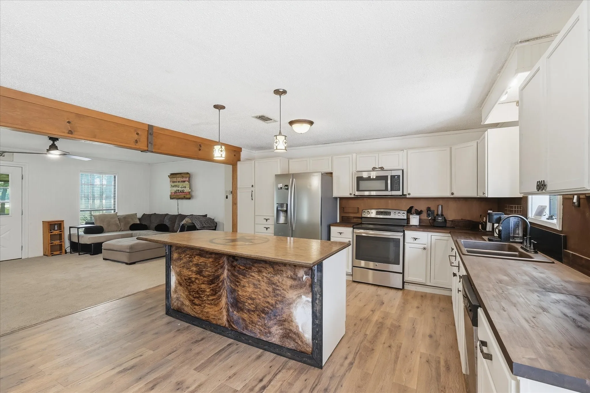 Kitchen featuring a central island, stainless steel appliances, wood-finish flooring, white cabinetry, and wood-toned countertops