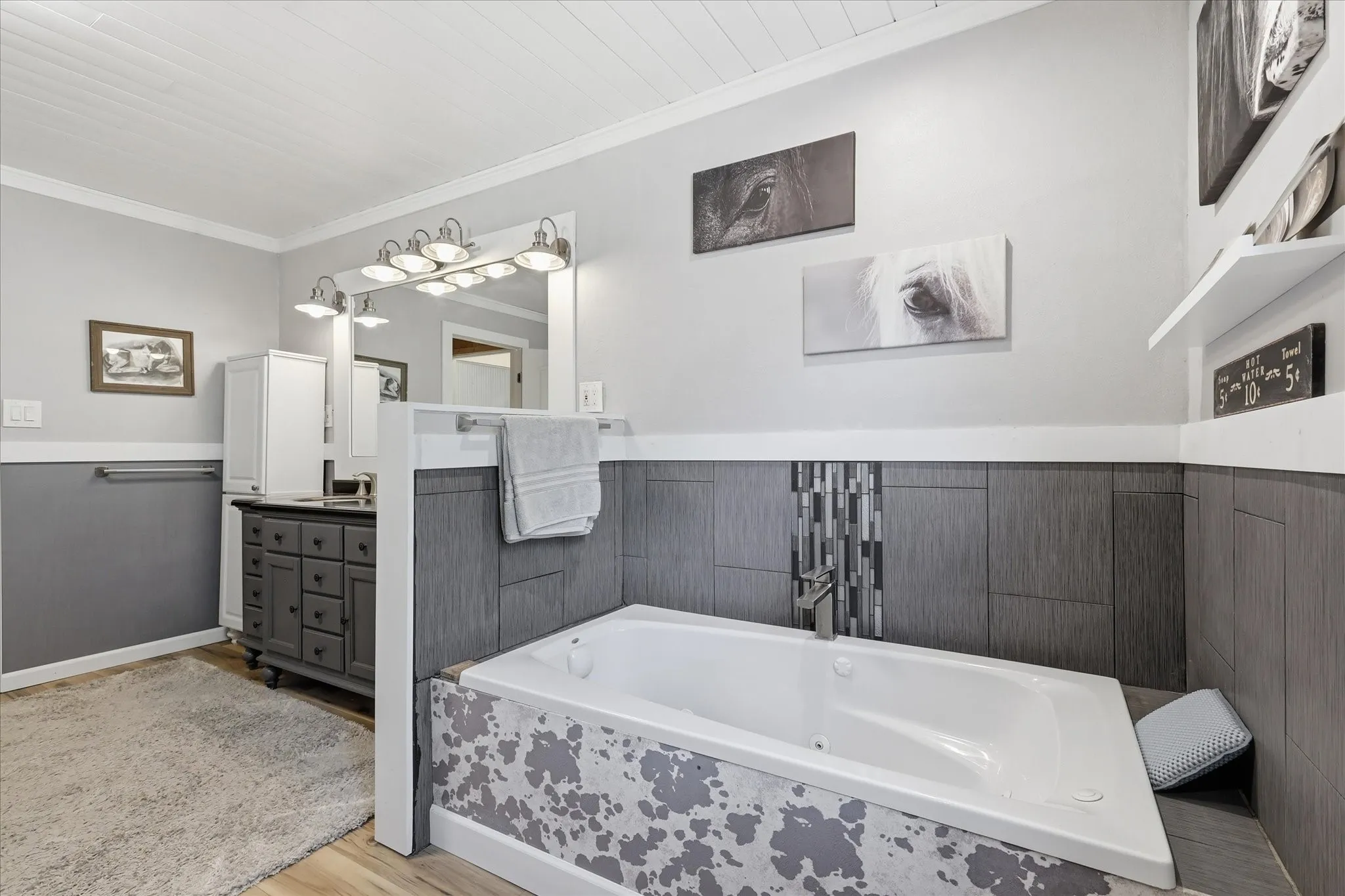 Bathroom featuring an inset bathtub with a tiled surround, a large vanity with a rectangular mirror, a paneled ceiling, and wood-finish flooring