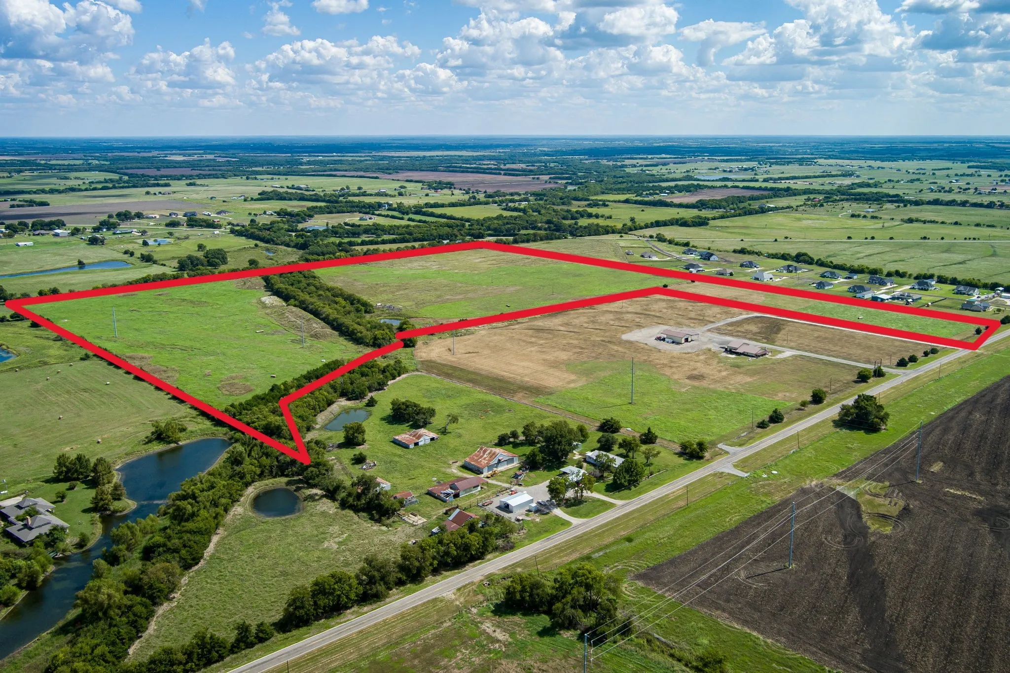 Expansive acreage featuring multiple ponds, mature trees, and open fields, bordered by a paved road