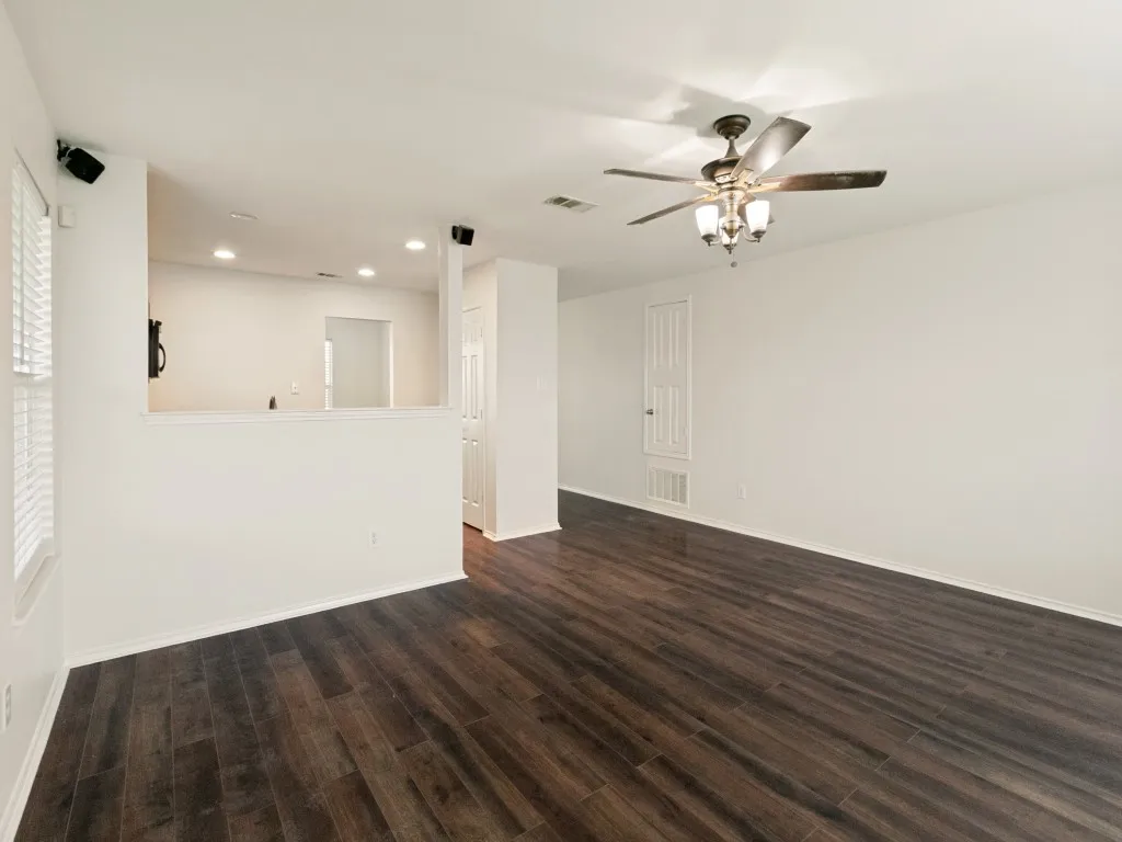 Spacious room featuring dark wood-finish flooring, white walls, and a ceiling fan with integrated lighting