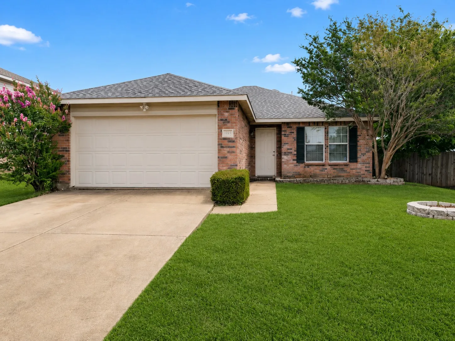 Brick facade residence featuring a two-car garage, concrete driveway, and a well-kept lawn