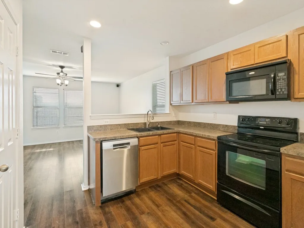 Kitchen featuring wood-finish flooring, light-toned cabinetry, dark countertops, and stainless steel dishwasher