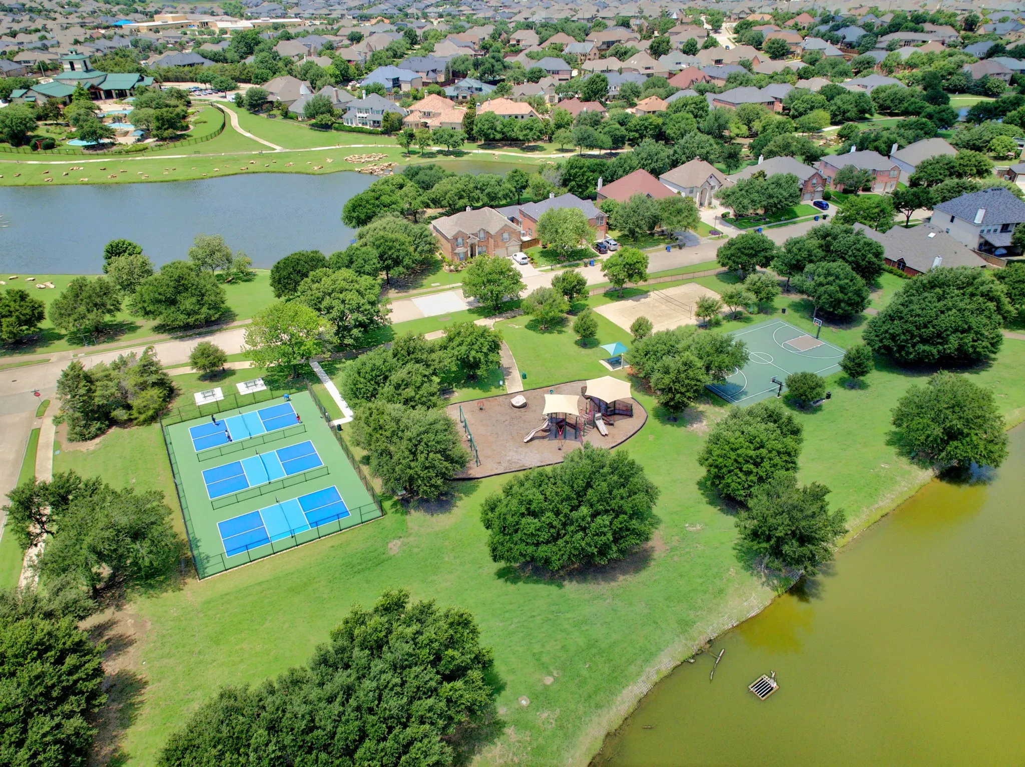 Expansive community amenities including multiple tennis courts, a basketball court, and a playground, all surrounded by green spaces and residential properties