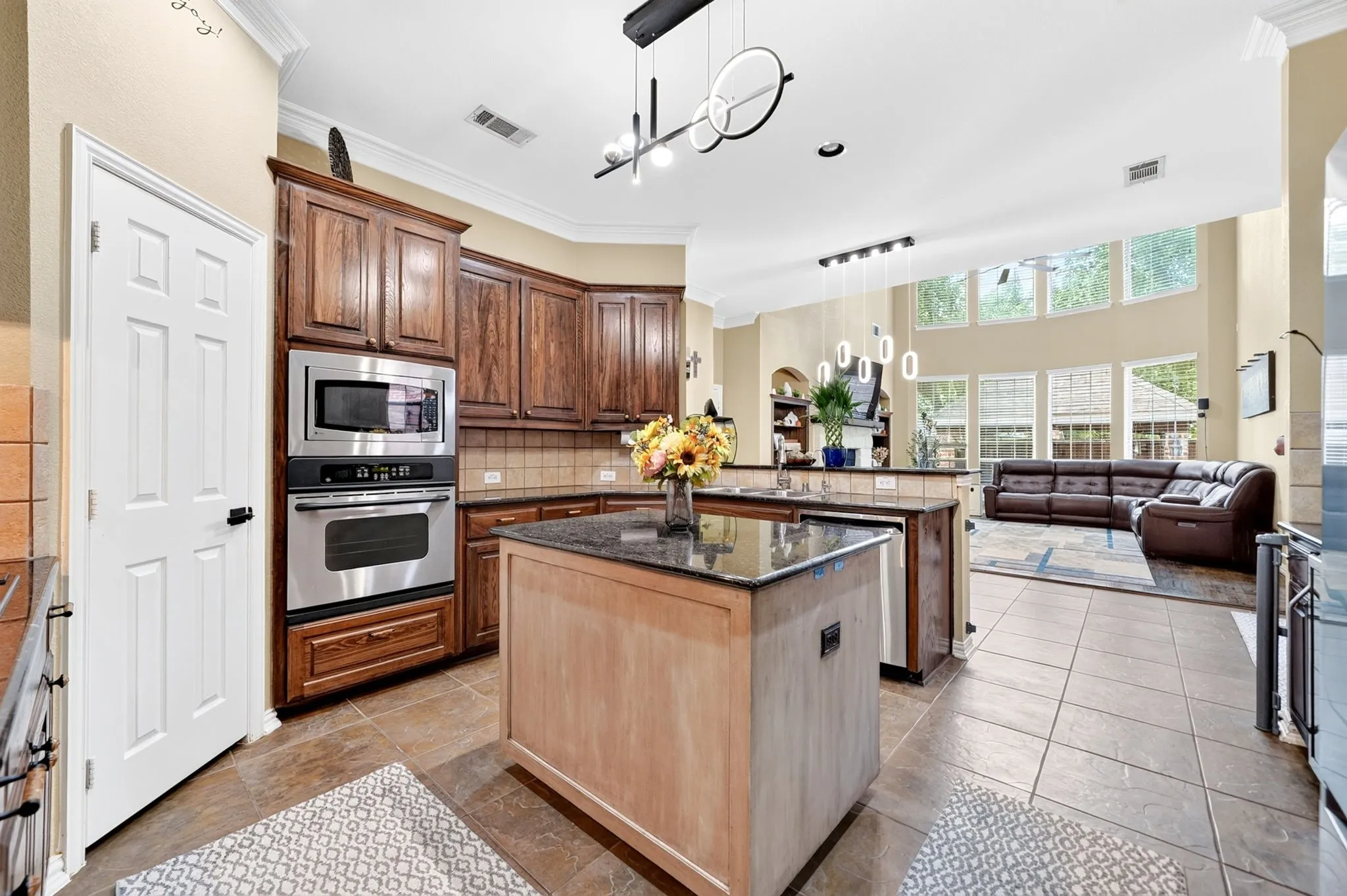 Open-concept kitchen featuring dark wood cabinetry, stainless steel appliances, a center island with a black countertop, and tile flooring