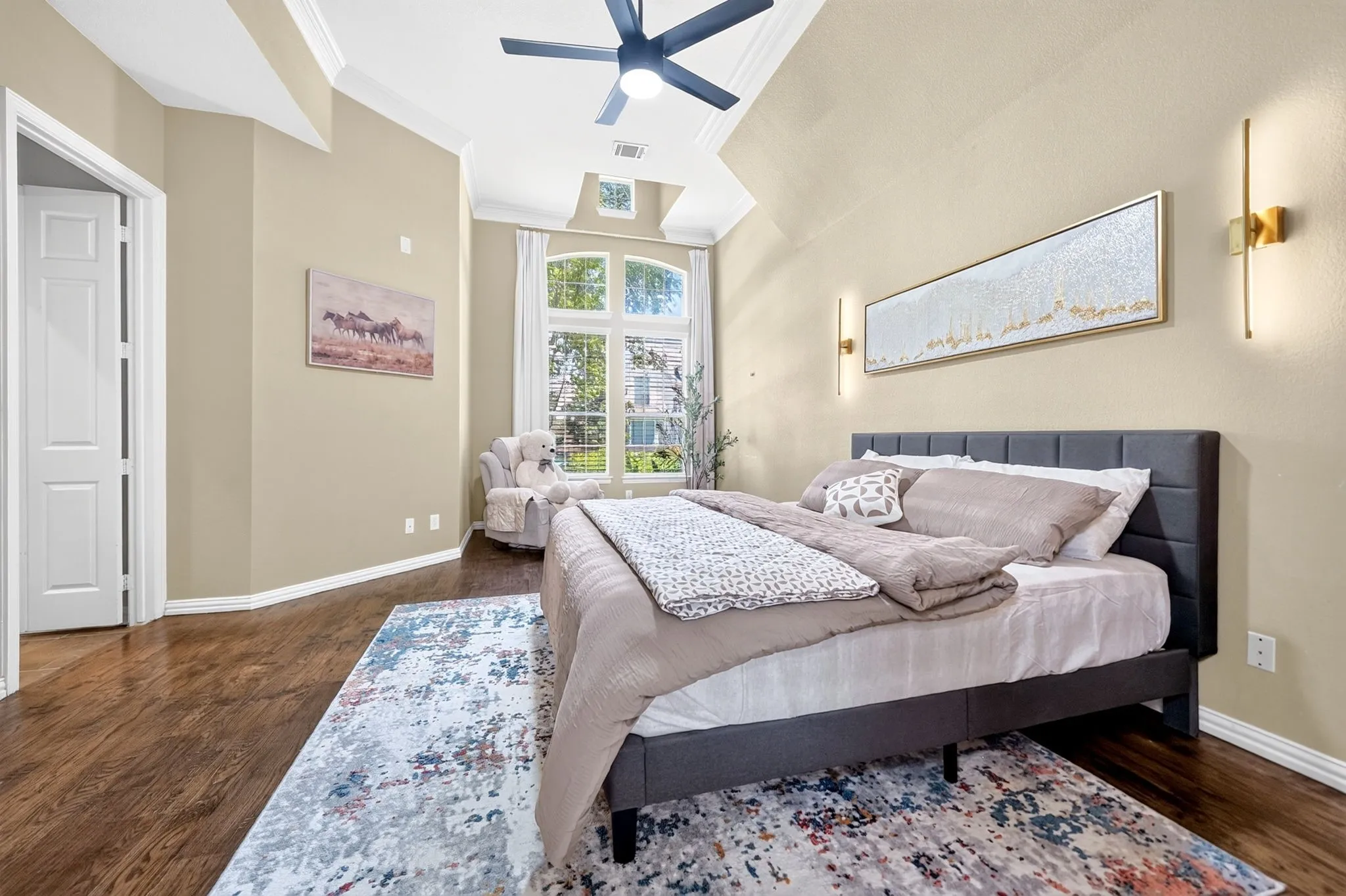 Spacious room featuring wood-finish flooring, vaulted ceilings with crown molding, and a ceiling fan