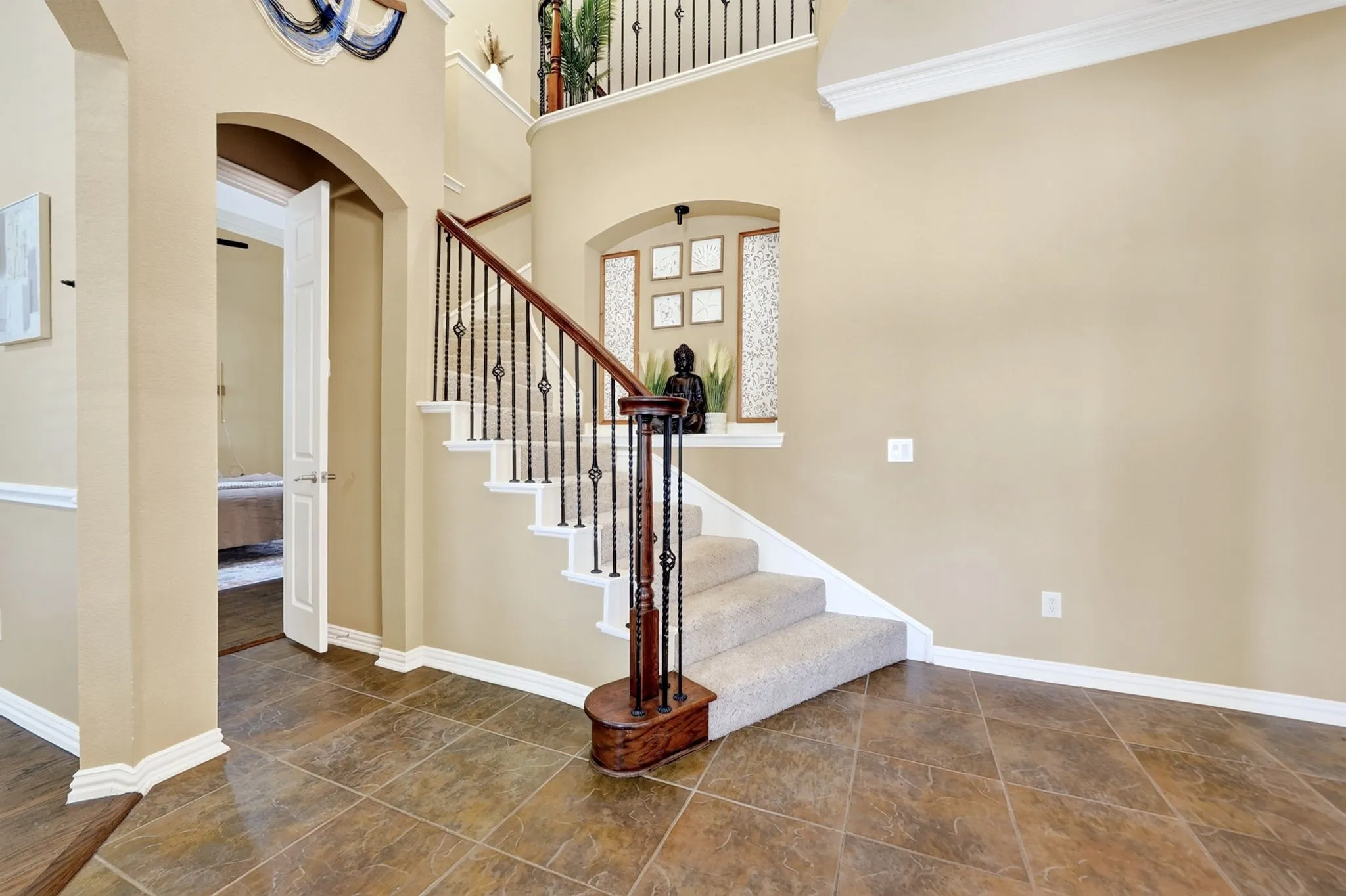 Two-story foyer featuring tile flooring, a carpeted staircase with dark wood handrails and wrought iron balusters, an arched doorway, and crown molding accents