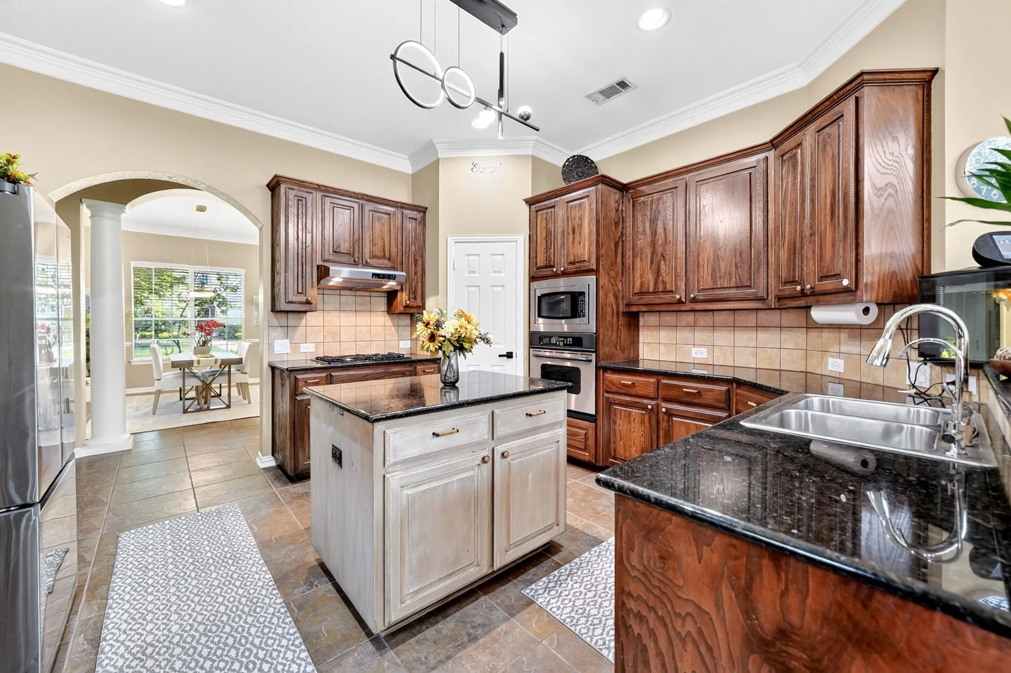 Gourmet kitchen featuring a central island, dark granite countertops, wood-finish cabinetry, stainless steel appliances, and tile flooring