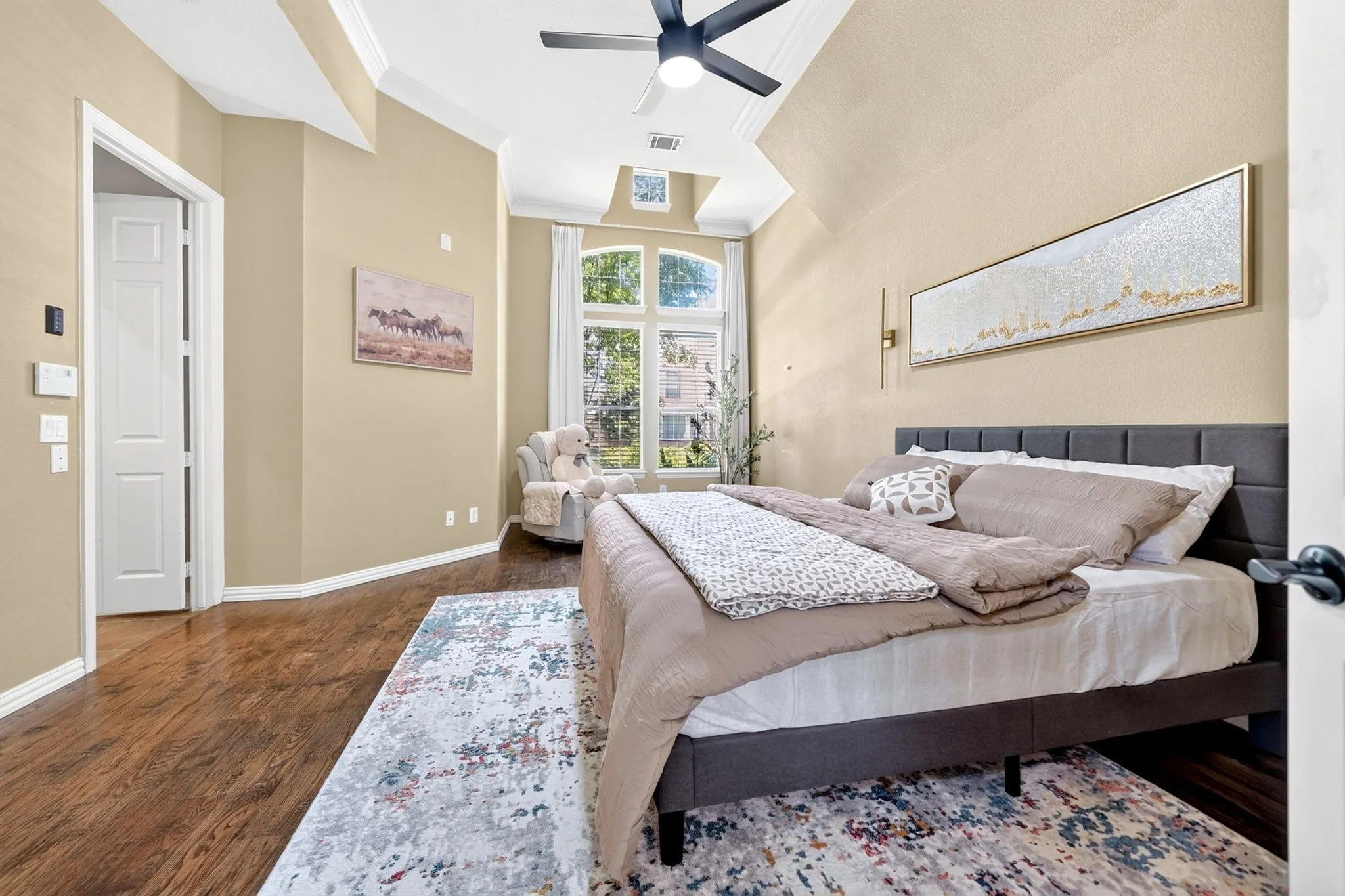 Spacious bedroom featuring wood-finish flooring, a tray ceiling, and a ceiling fan