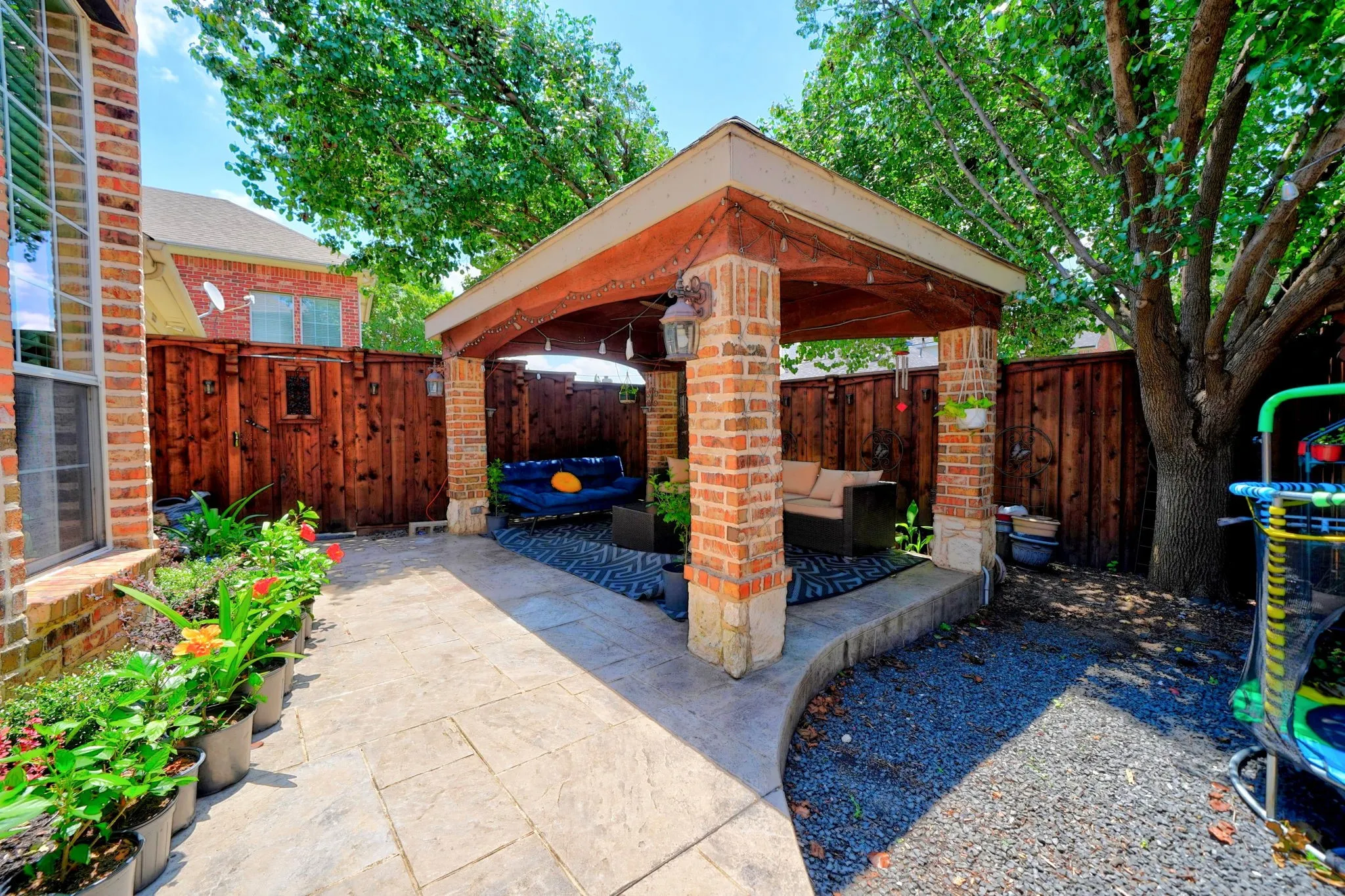 Brick-columned outdoor pavilion with a wood-finish ceiling, stone base accents, and overhead lighting