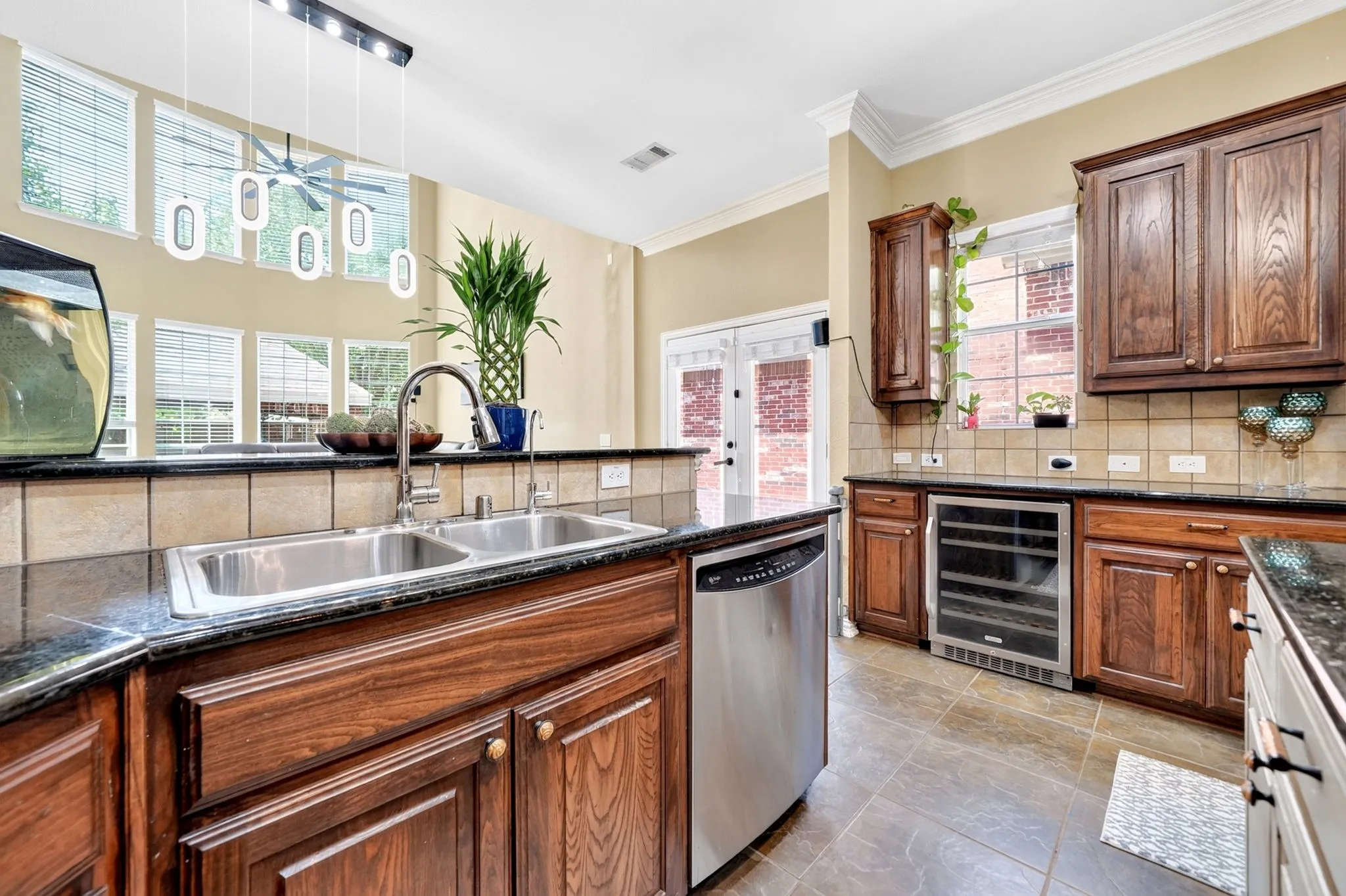 Kitchen featuring a dual basin stainless steel sink, dark wood cabinetry, granite-finish countertops, and a built-in beverage refrigerator
