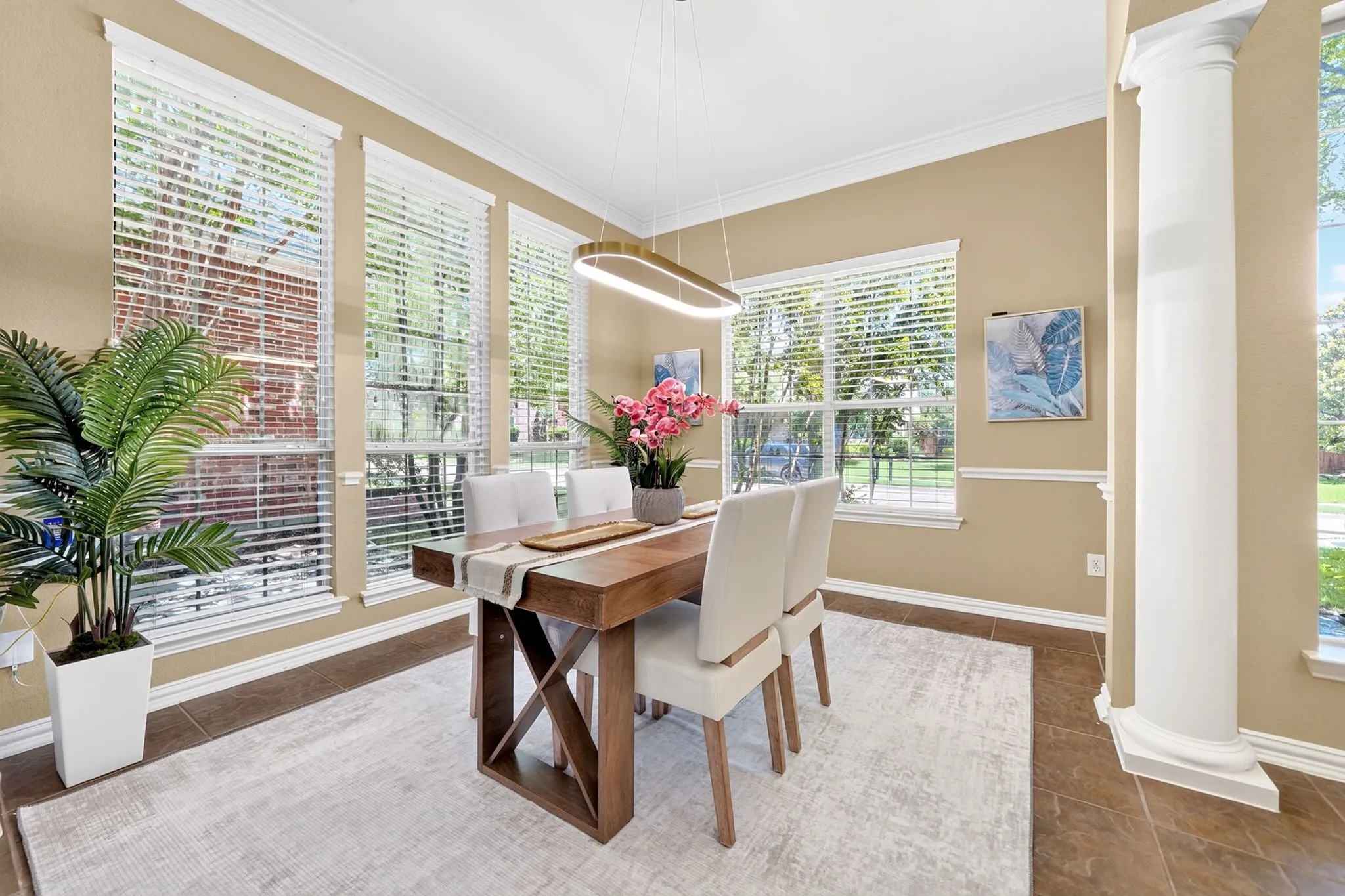 Formal dining area featuring multiple large windows with blinds, a prominent architectural column, crown molding, and tiled flooring