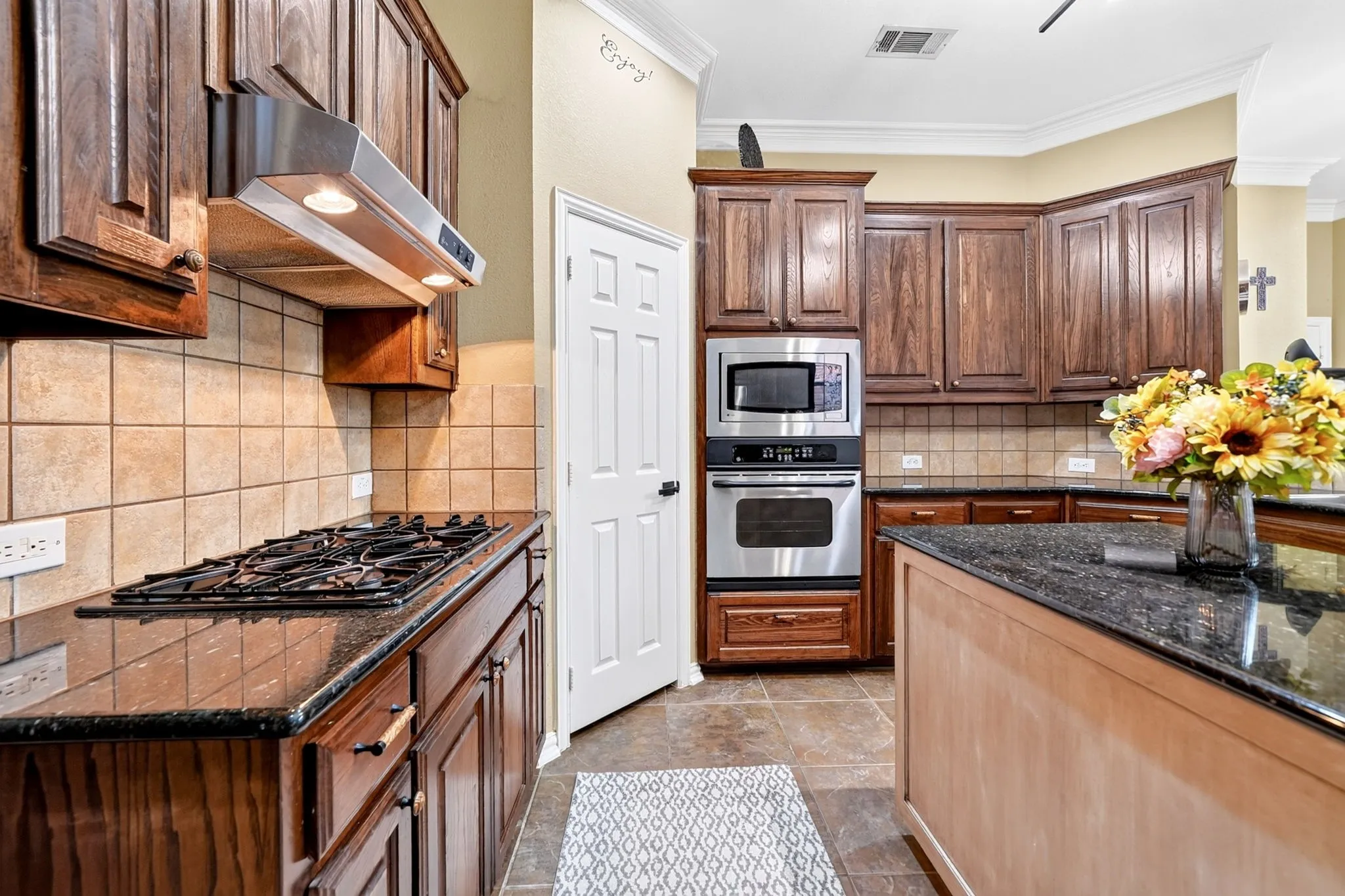 Kitchen featuring rich wood cabinetry, dark countertops, a built-in wall oven and microwave, a gas cooktop, and a tile backsplash