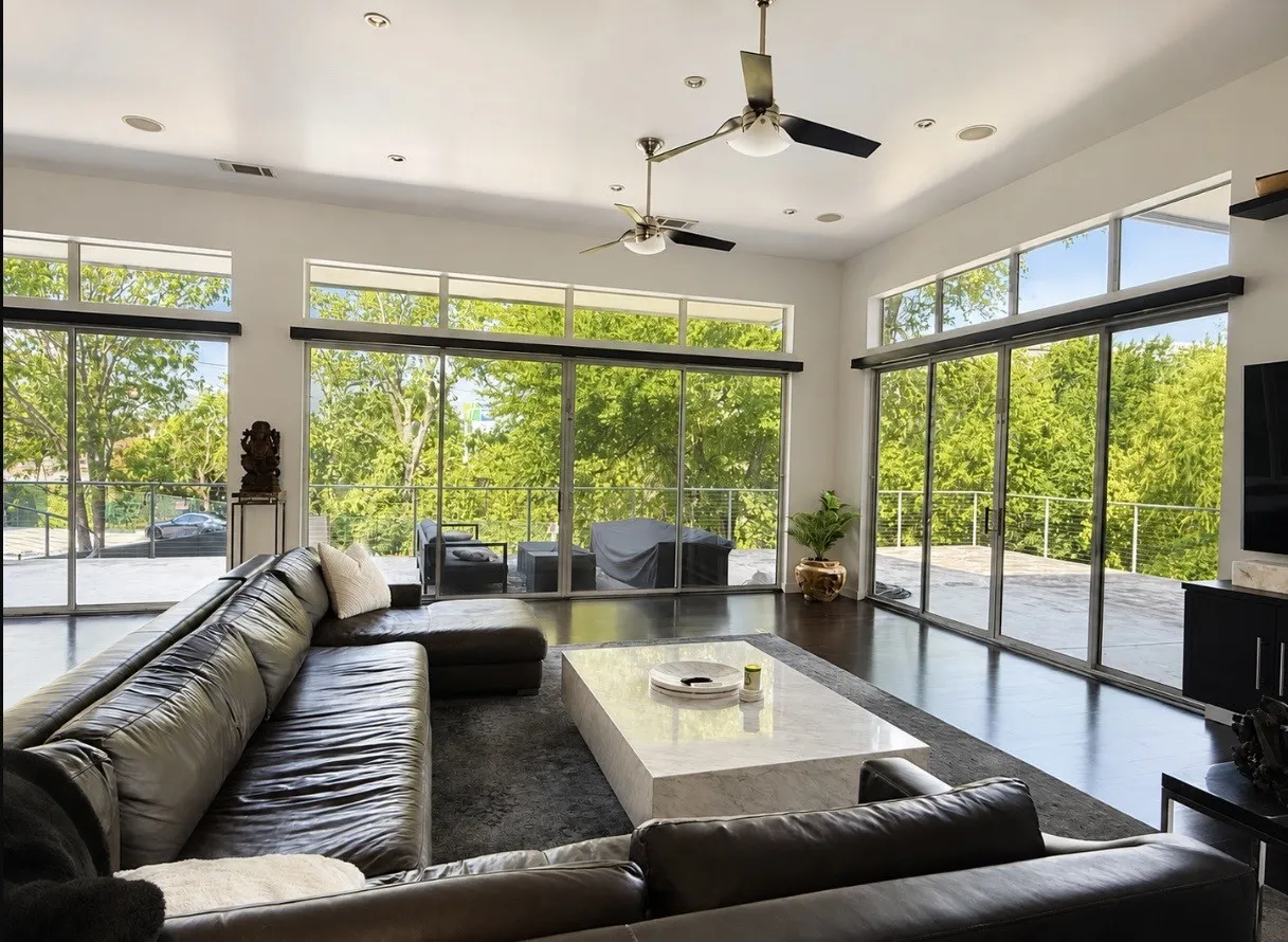 Expansive living area with high ceilings, recessed lighting, polished wood-finish flooring, and multiple sliding glass doors leading to an outdoor deck