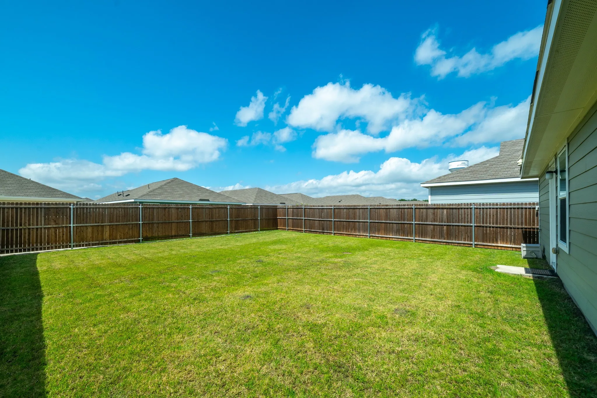 Expansive backyard featuring a green lawn, wood privacy fencing, and a light-colored siding exterior