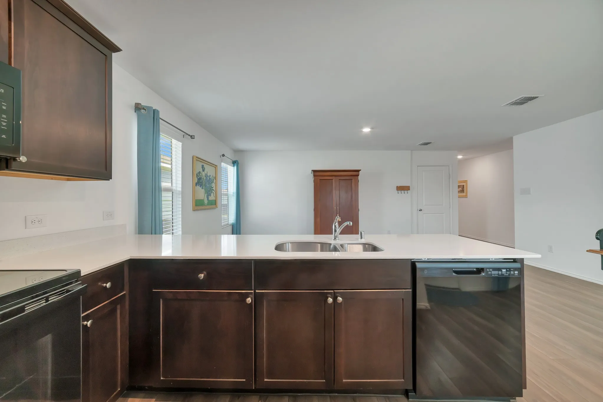 Kitchen island with a double basin sink, white countertops, dark wood-finish cabinetry, and an integrated dishwasher