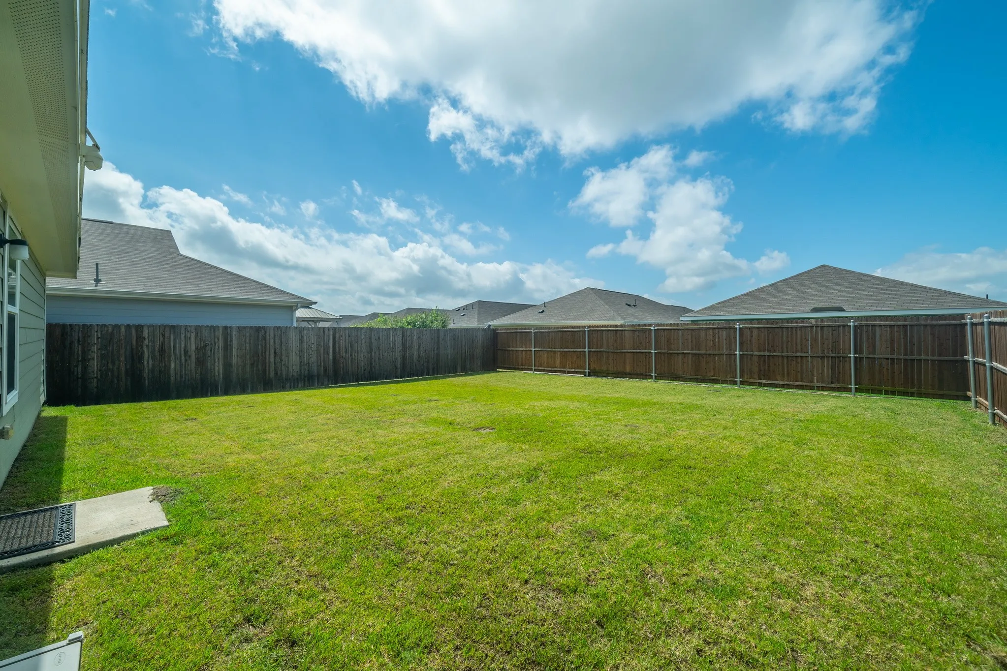 Expansive backyard featuring a manicured lawn, full wood privacy fencing, and a concrete patio pad