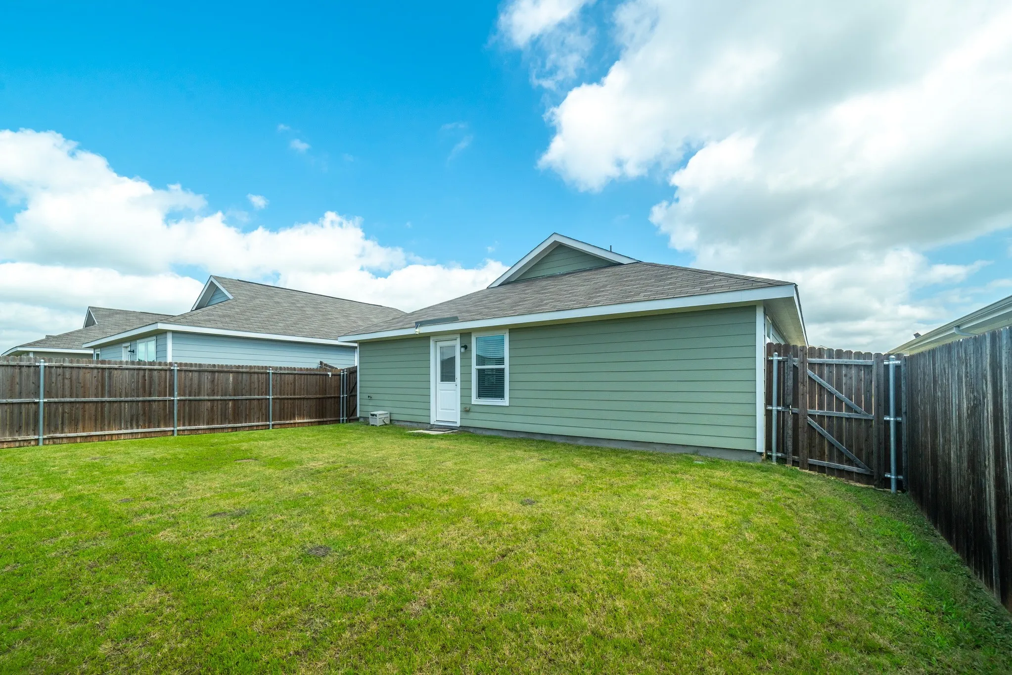 Expansive backyard featuring a lush lawn, privacy fencing, and a rear exterior door