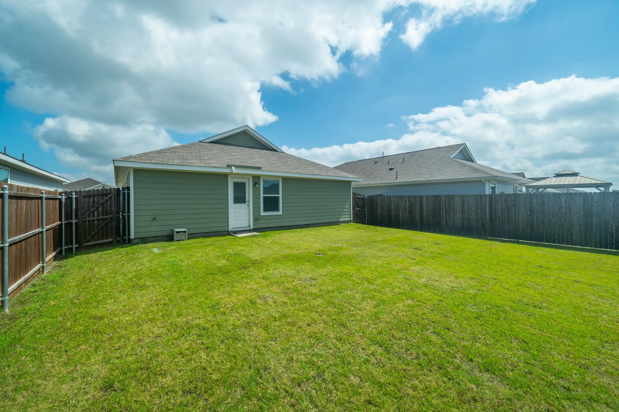 Expansive rear lawn featuring a privacy fence, wood-paneled siding, a back entrance, and a gabled roofline