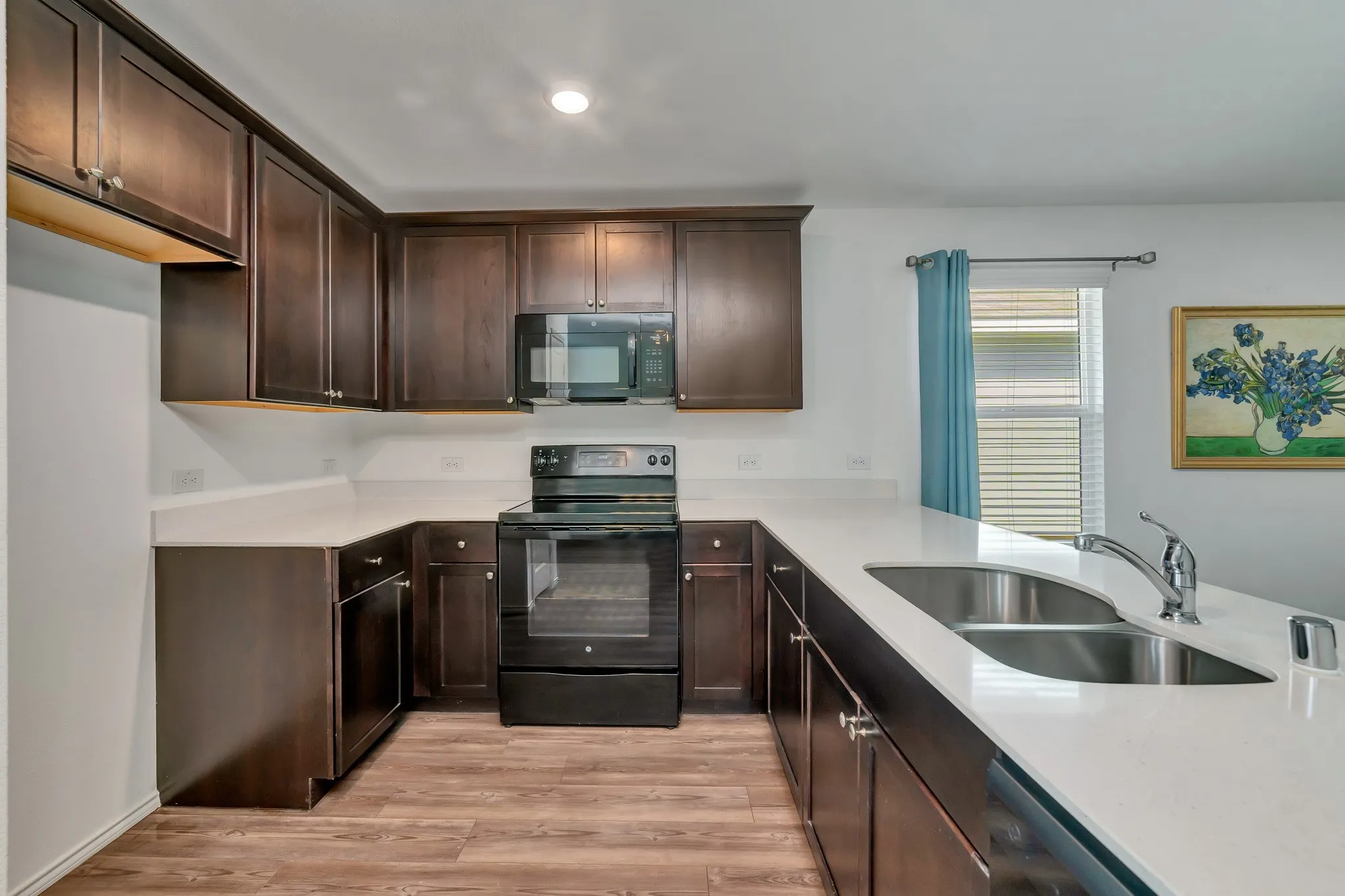 Kitchen featuring dark wood cabinetry, light-toned countertops, a stainless steel double-basin sink with a chrome faucet, black electric range, and wood-finish flooring