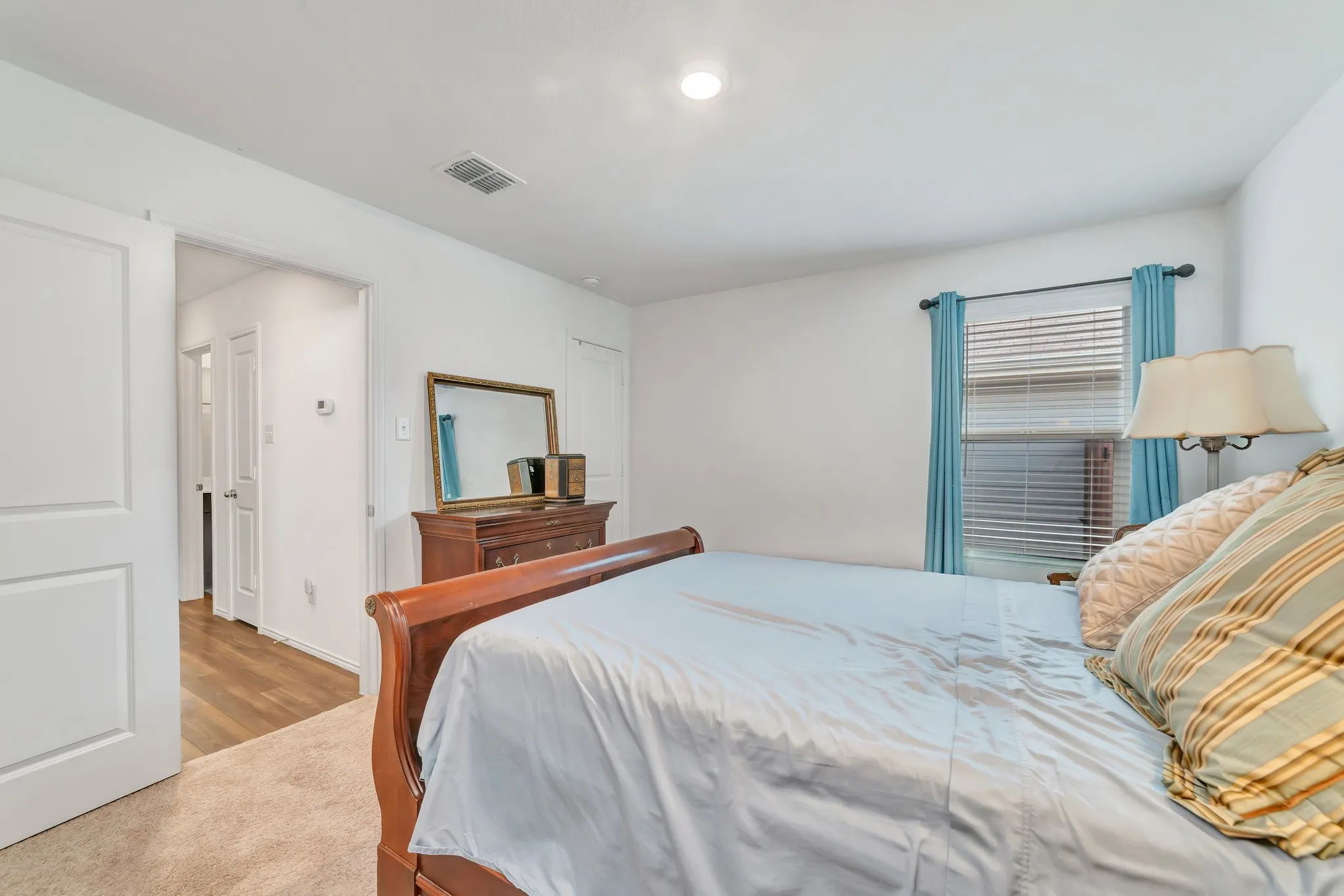 Carpeted room with a single window featuring horizontal blinds and blue fabric curtains