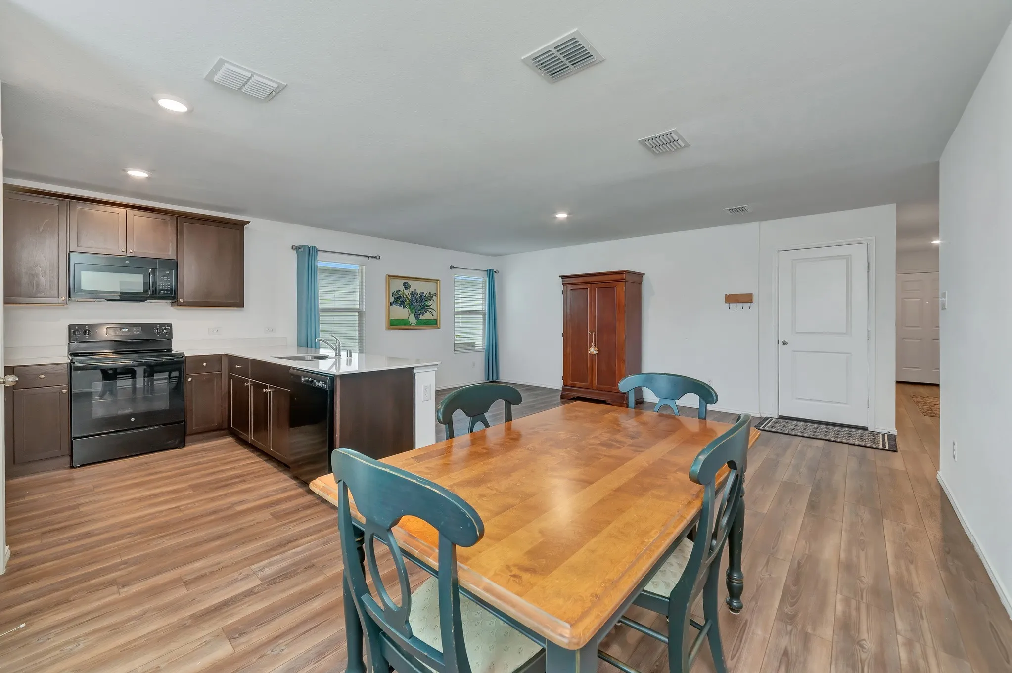 Open-concept living area featuring wood-finish flooring, recessed lighting, white walls, dark wood cabinetry, and a kitchen island with a sink