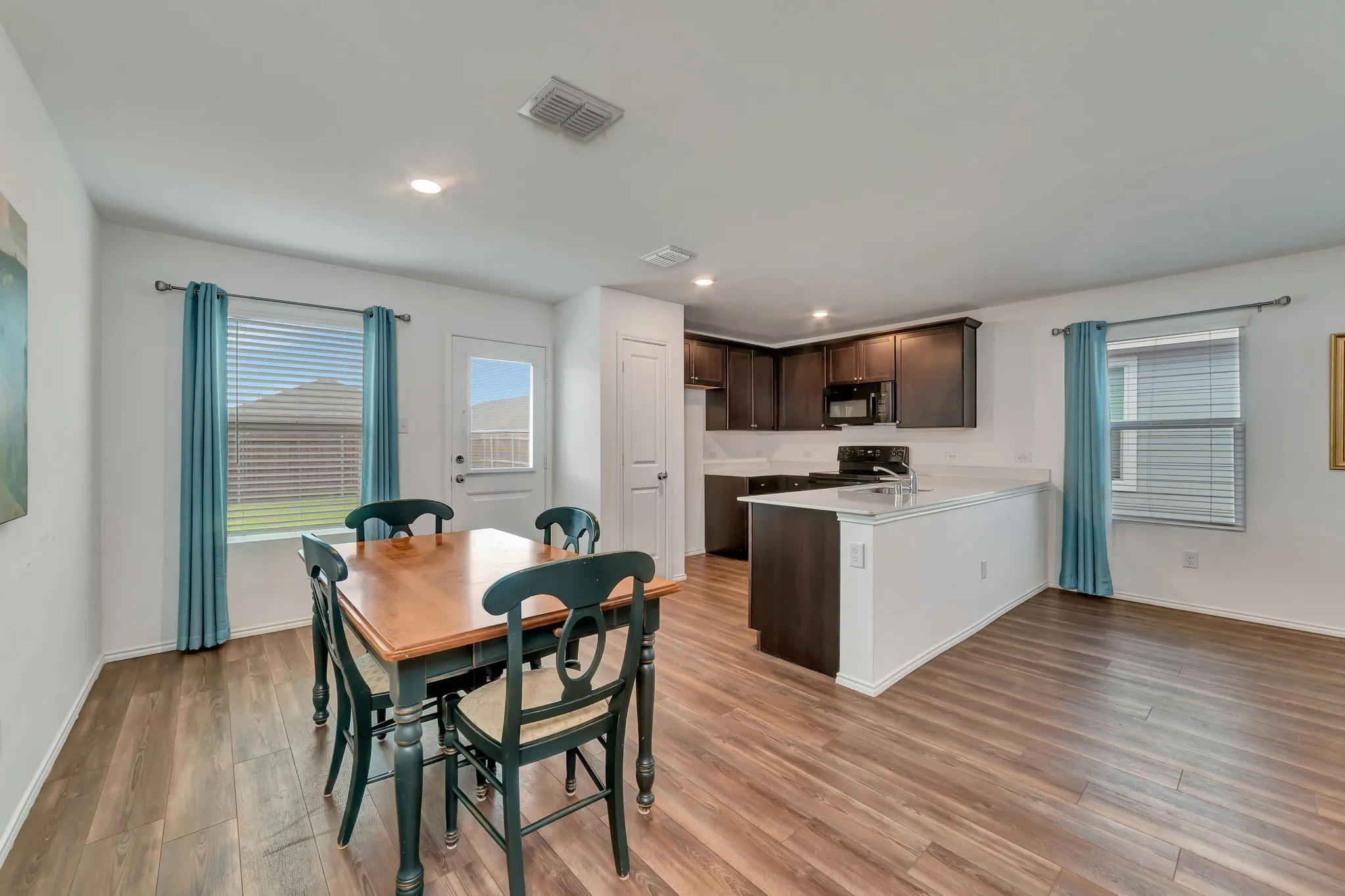 Open-concept kitchen and dining area featuring wood-finish flooring, recessed lighting, dark wood-finish cabinetry, and white countertops