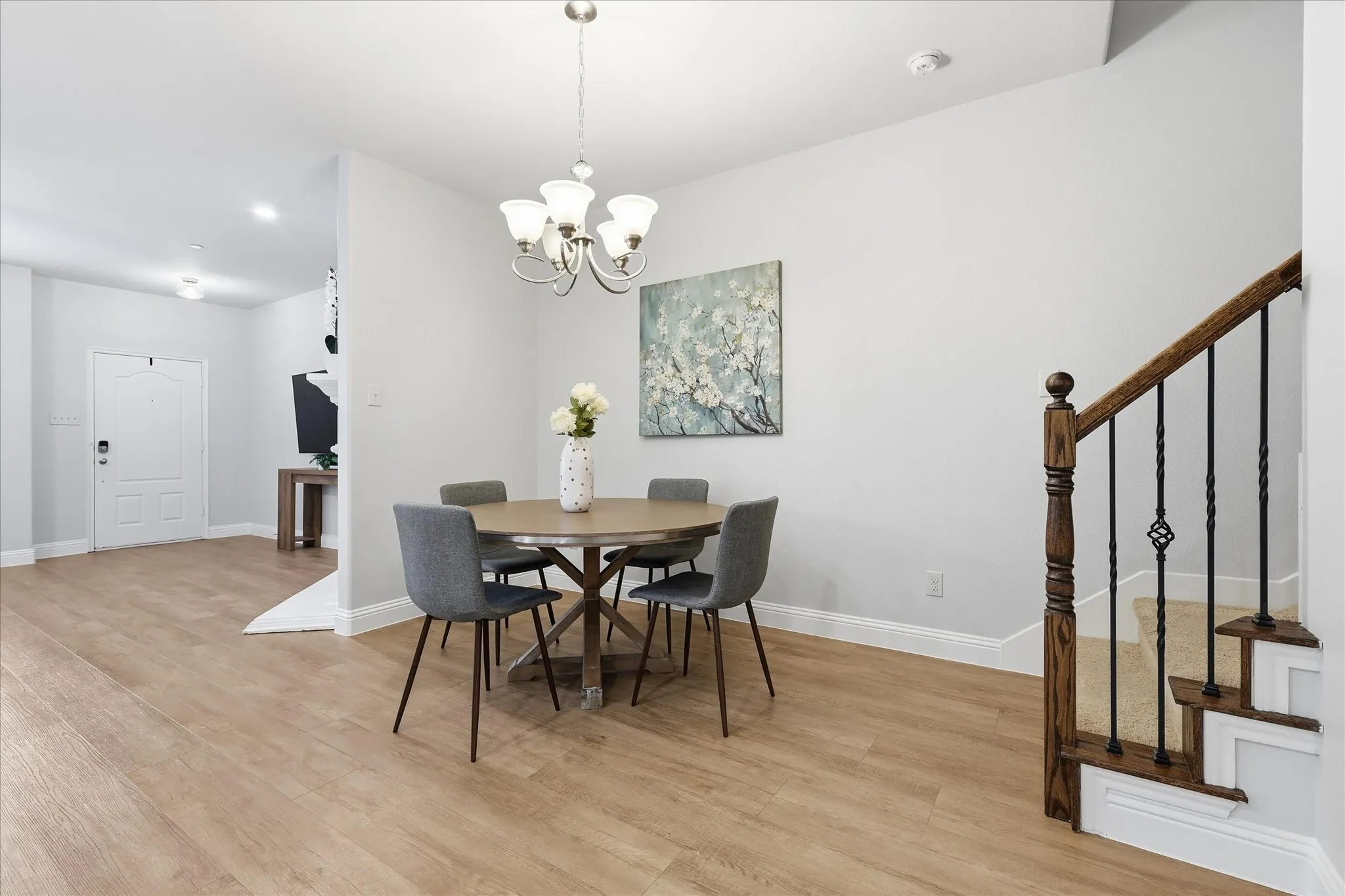 Open-concept dining area featuring wood-finish flooring, a contemporary chandelier, and a white paneled door