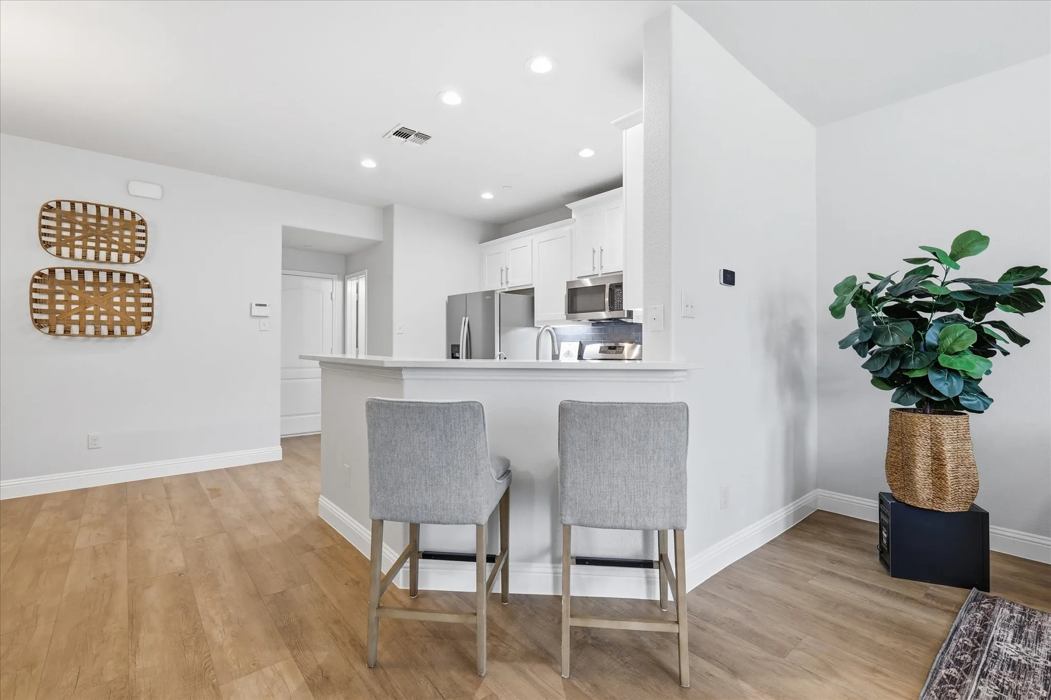 Open-concept kitchen featuring a breakfast bar with seating, stainless steel appliances, white cabinetry, recessed lighting, and wood-finish flooring