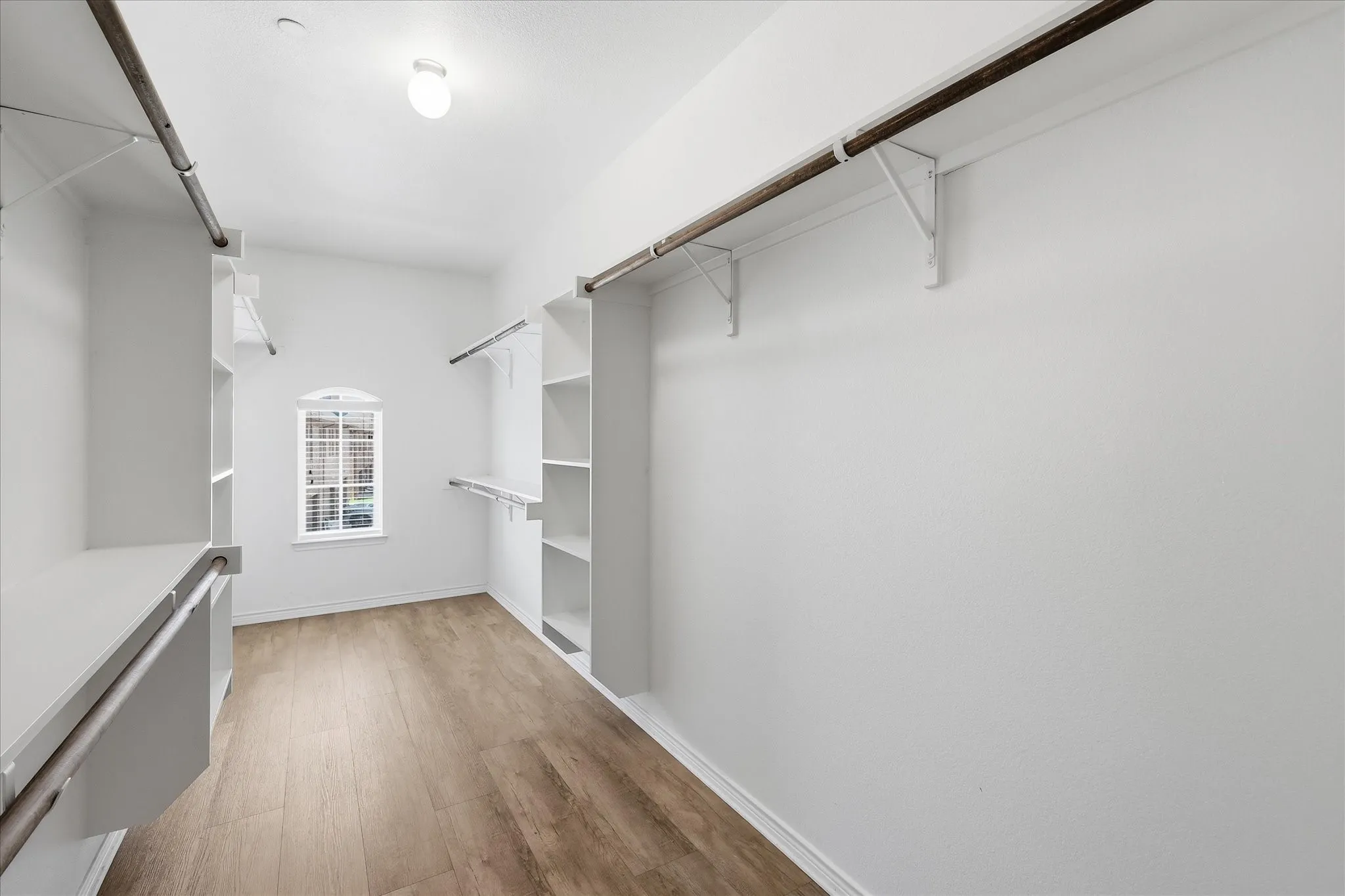 Spacious walk-in closet featuring wood-finish flooring, white walls, and built-in shelving units