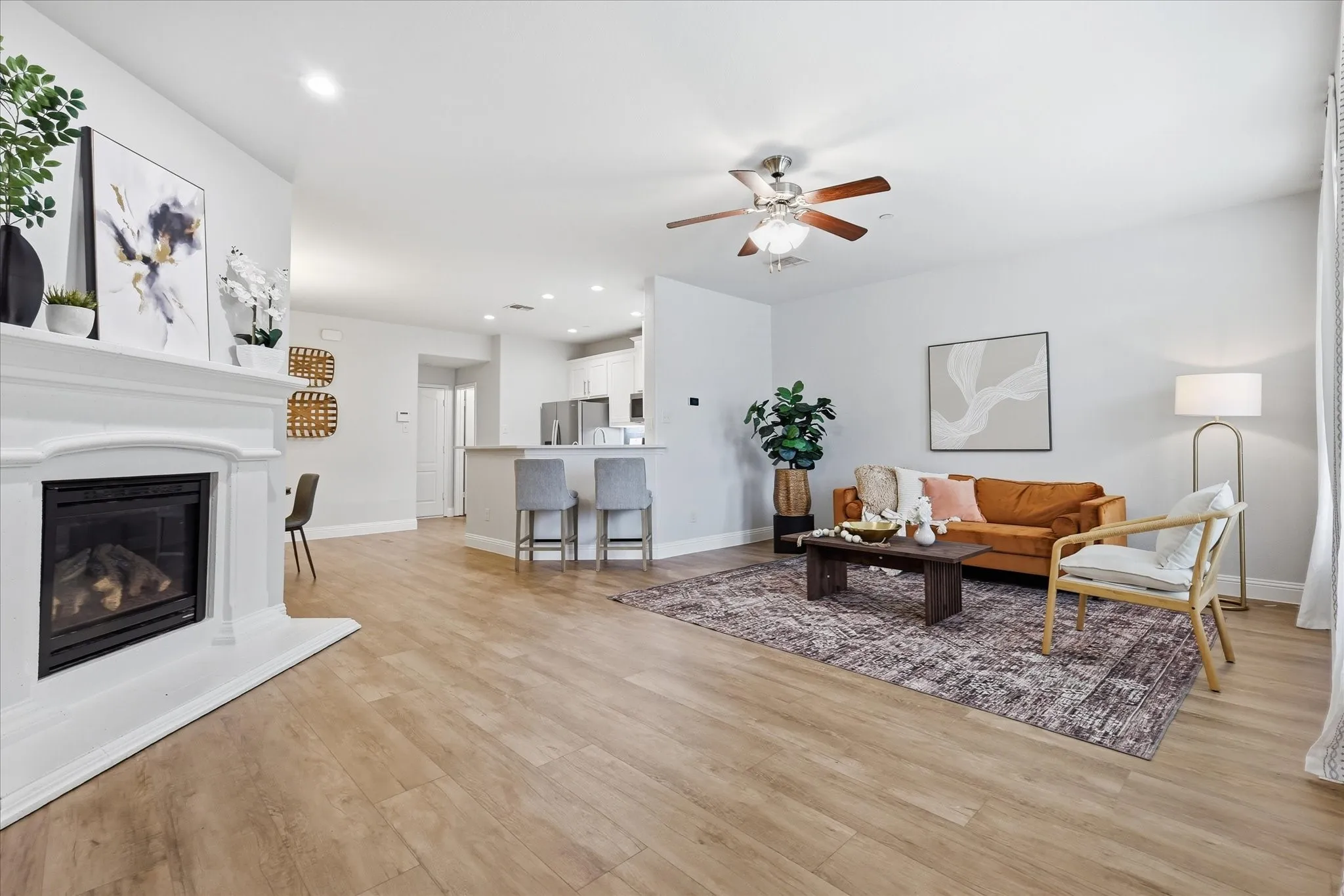 Spacious living area featuring light wood-finish flooring, a white fireplace with a mantel, and recessed lighting