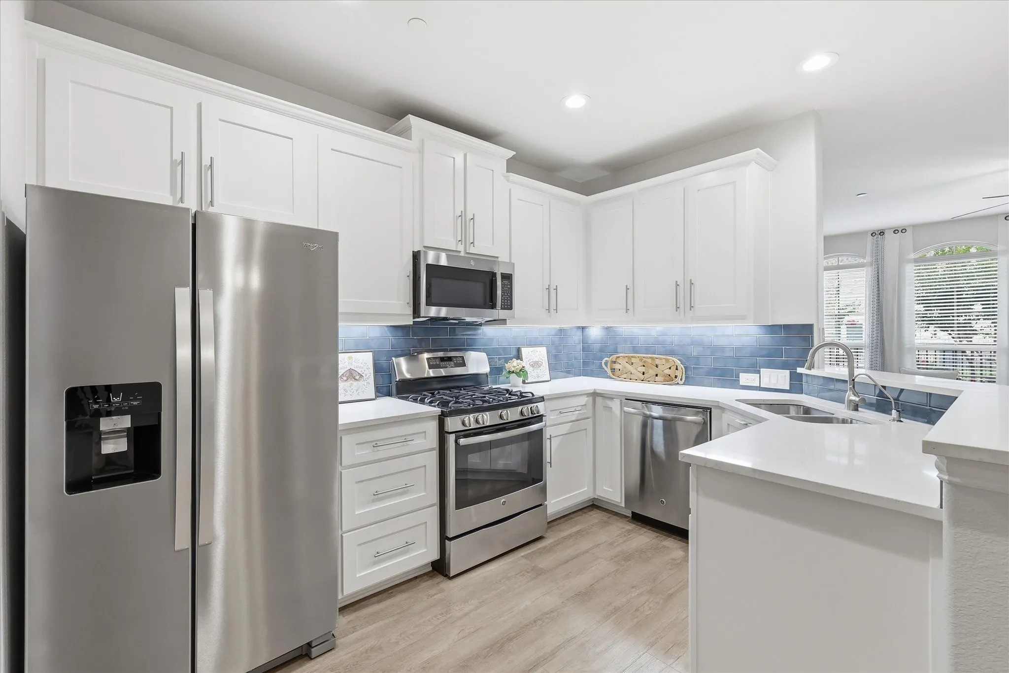 Kitchen featuring white cabinetry, stainless steel appliances, a blue subway tile backsplash, light countertops, and wood-finish flooring