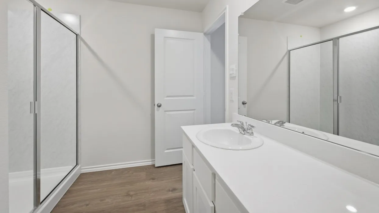 Bathroom featuring a single vanity with a white countertop and oval undermount sink, chrome faucet, wood-finish flooring, and a glass-enclosed shower
