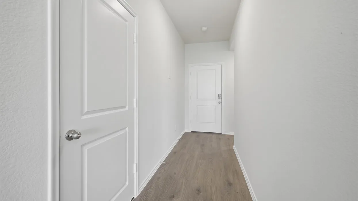 Hallway featuring wood-finish flooring, white walls, and a two-panel interior door with a chrome knob