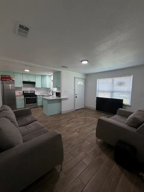 Open-concept living space featuring wood-finish flooring, recessed lighting, and a kitchen with light blue cabinetry, stainless steel appliances, and a breakfast bar