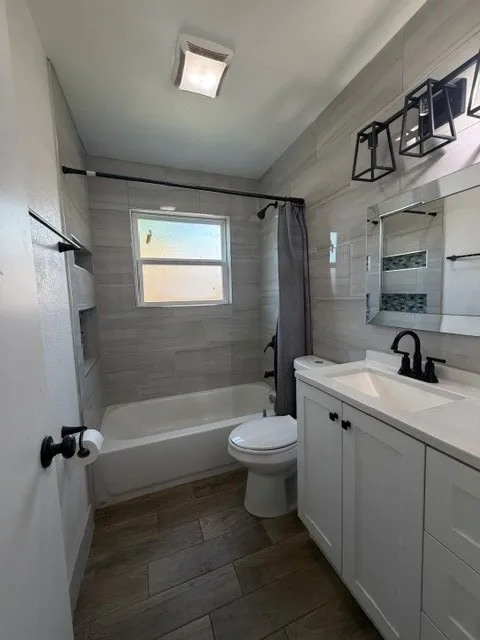 Bathroom featuring a white vanity with integrated sink, dark wood-finish tile flooring, a white bathtub with tile surround, a window, and modern black light fixture