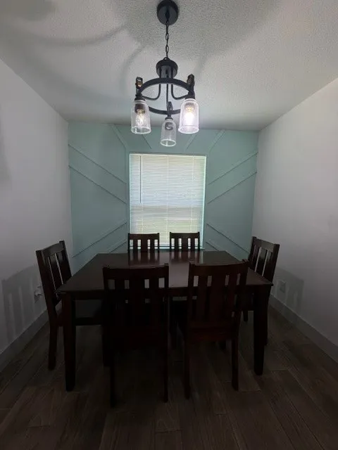 Dining area featuring a decorative accent wall with geometric paneling, wood-finish flooring, and a contemporary chandelier with clear glass shades