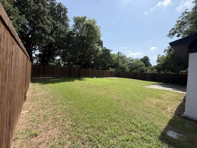 Expansive fenced backyard featuring a grassy lawn, mature perimeter trees, and a partial concrete patio