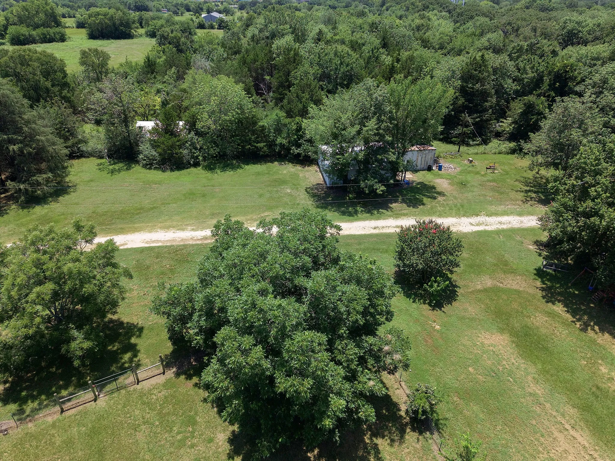 Expansive green acreage featuring mature trees and a gravel driveway fence divides