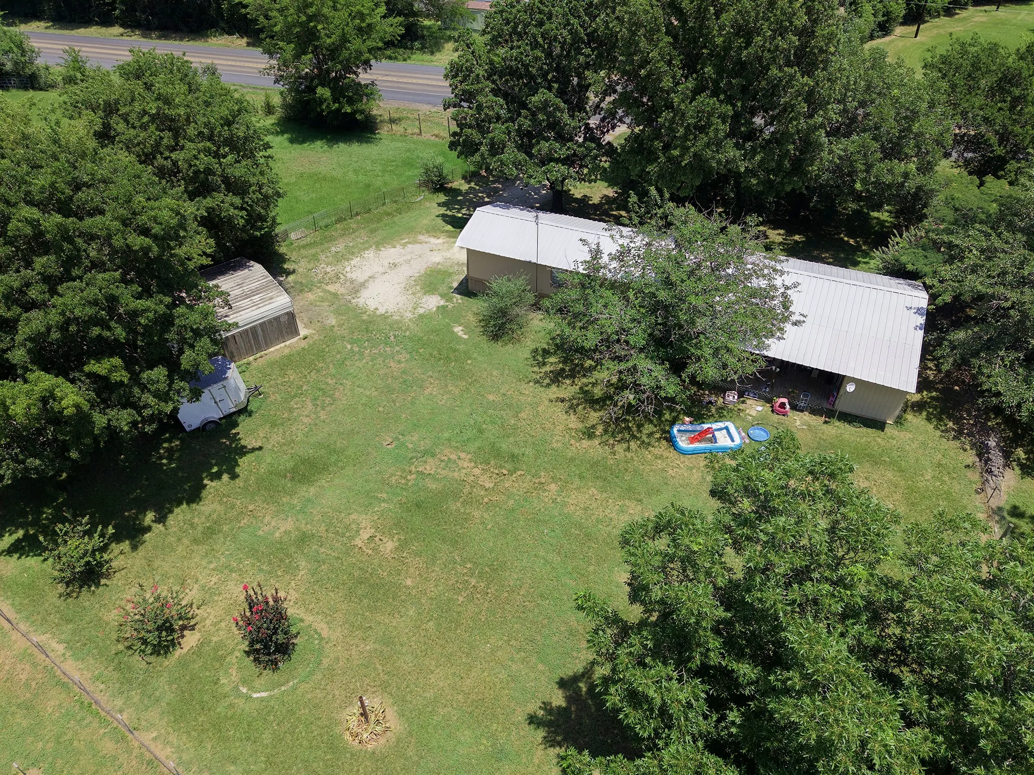Expansive green lot featuring a single-story structure with a metal roof and a separate carpot