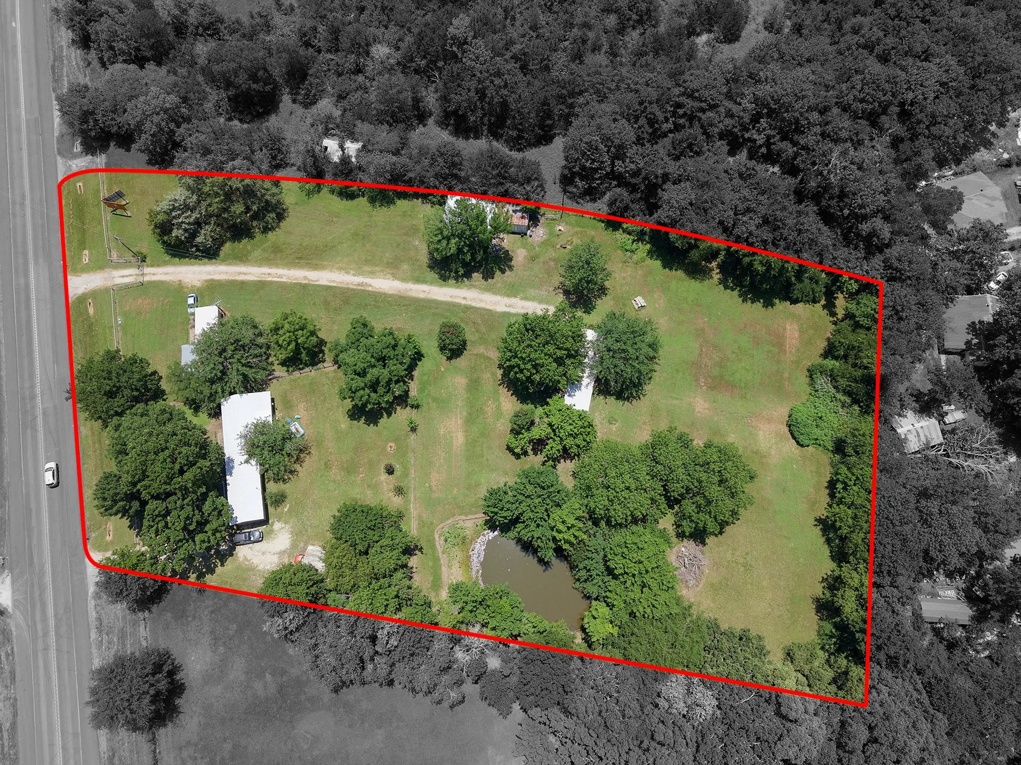 Expansive property featuring a road frontage, multiple structures, a private pond, and mature tree coverage