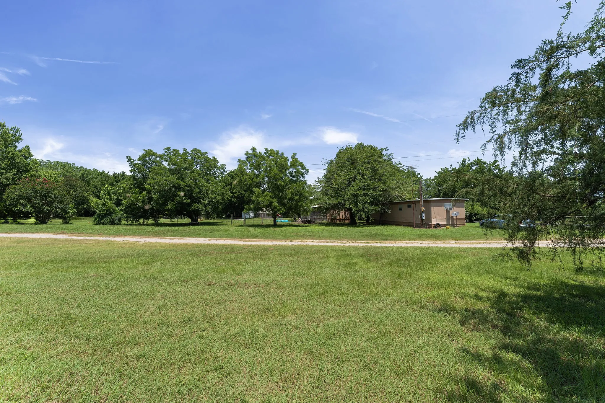 Expansive grassy lot with mature perimeter trees and a natural dirt path