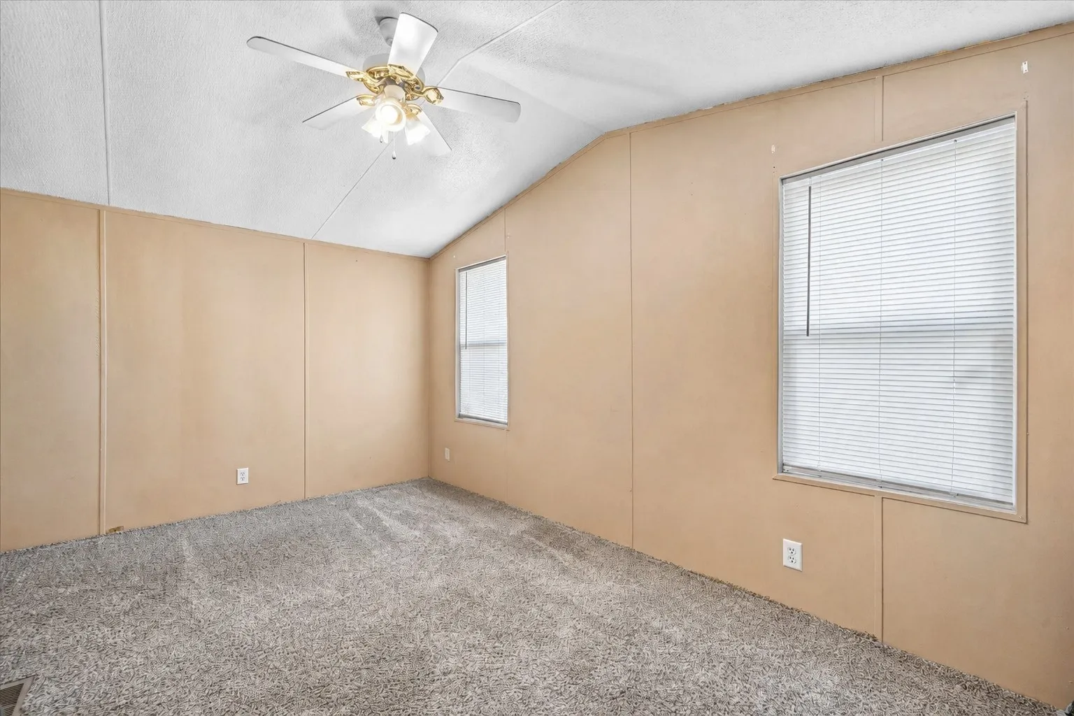 Room featuring sloped ceilings, two windows with horizontal blinds, and paneled walls