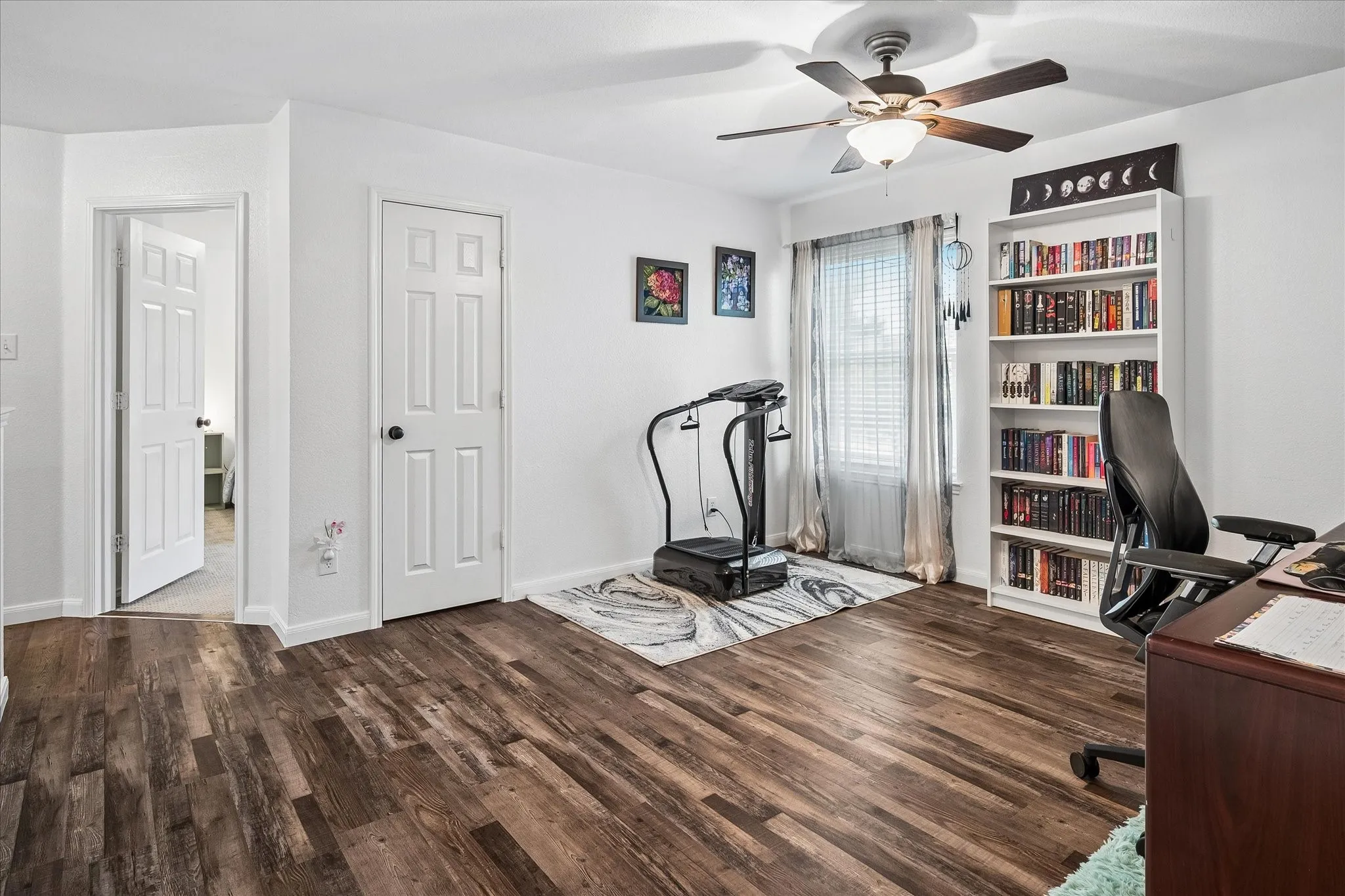 Wood-finish flooring, white paneled doors, ceiling fan with integrated lighting, and a prominent window with blinds