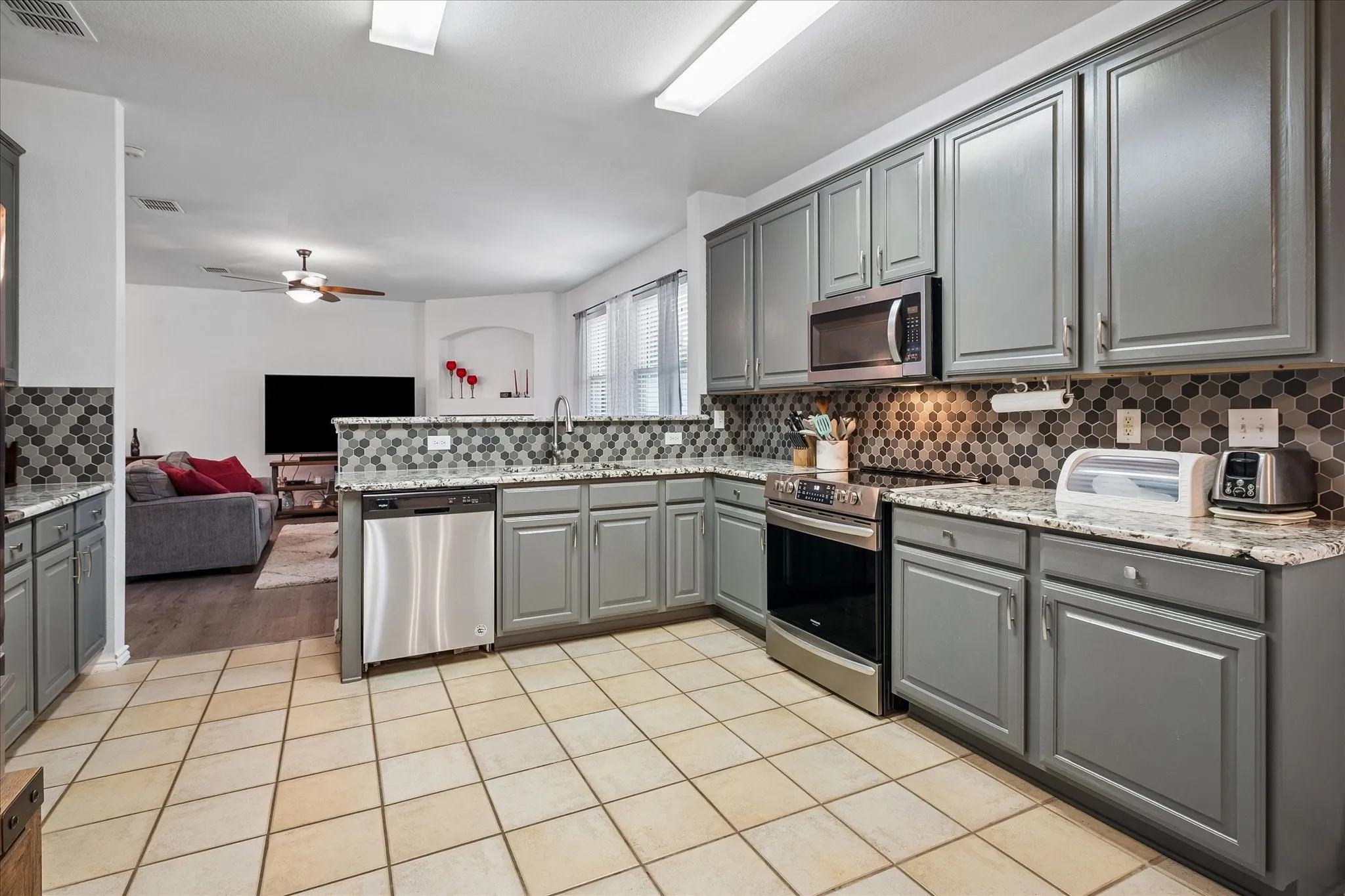 Kitchen featuring stainless steel appliances, grey cabinetry, mosaic tile backsplash, and light-toned tile flooring
