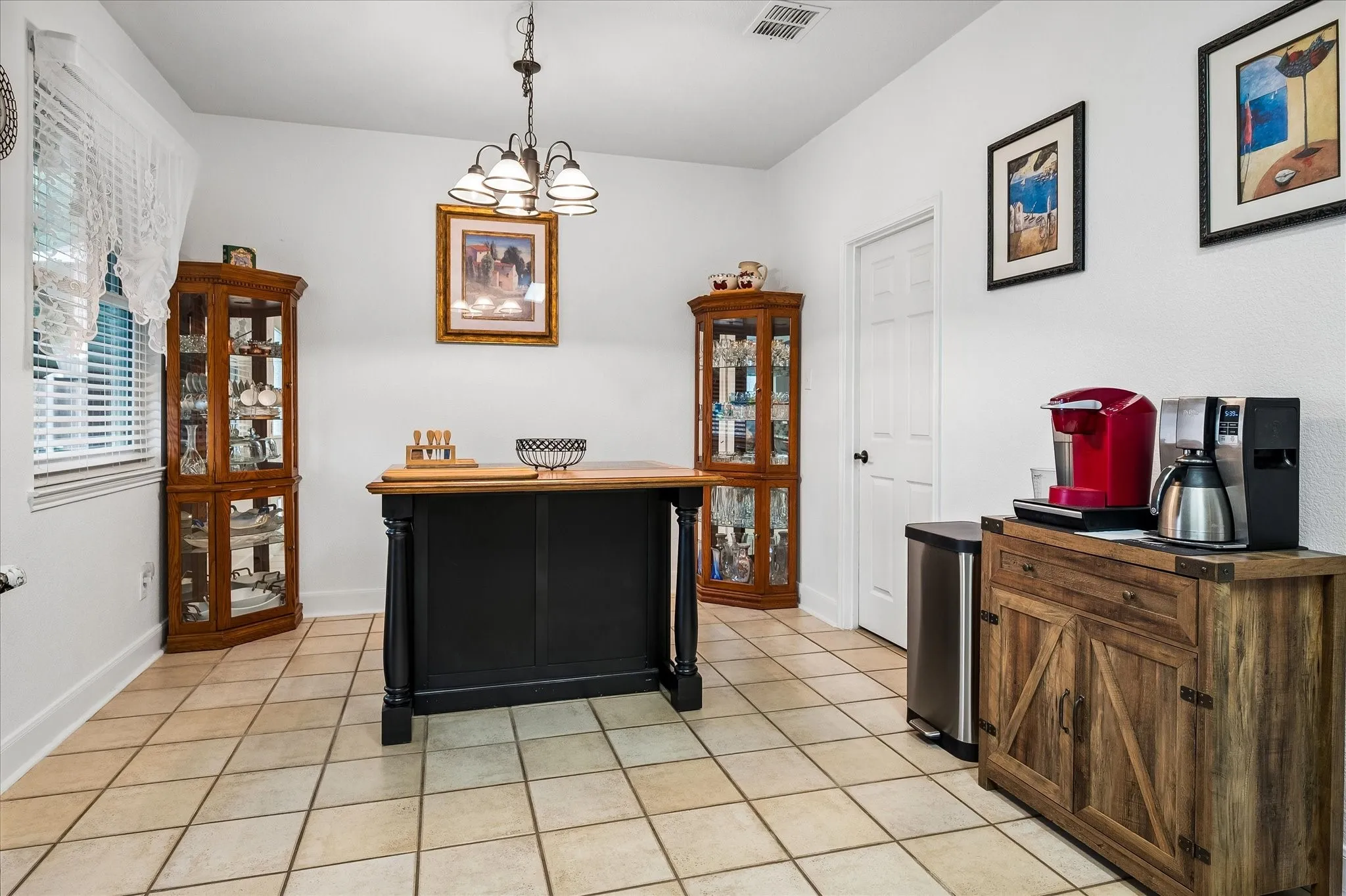 White walls with a single window featuring blinds, a central island with a wood-finish countertop, and tile flooring