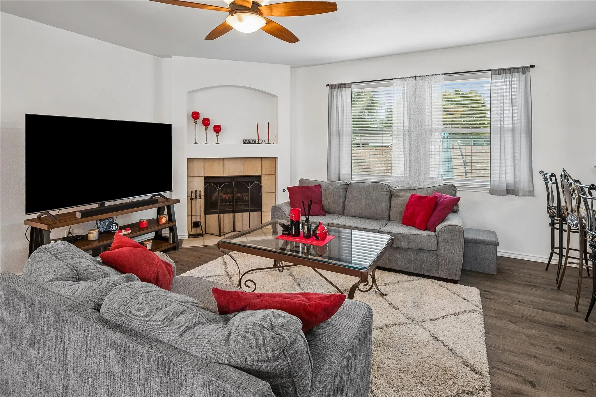 Corner fireplace with arched built-in shelving, wood-finish flooring, ceiling fan with integrated lighting, and multiple windows