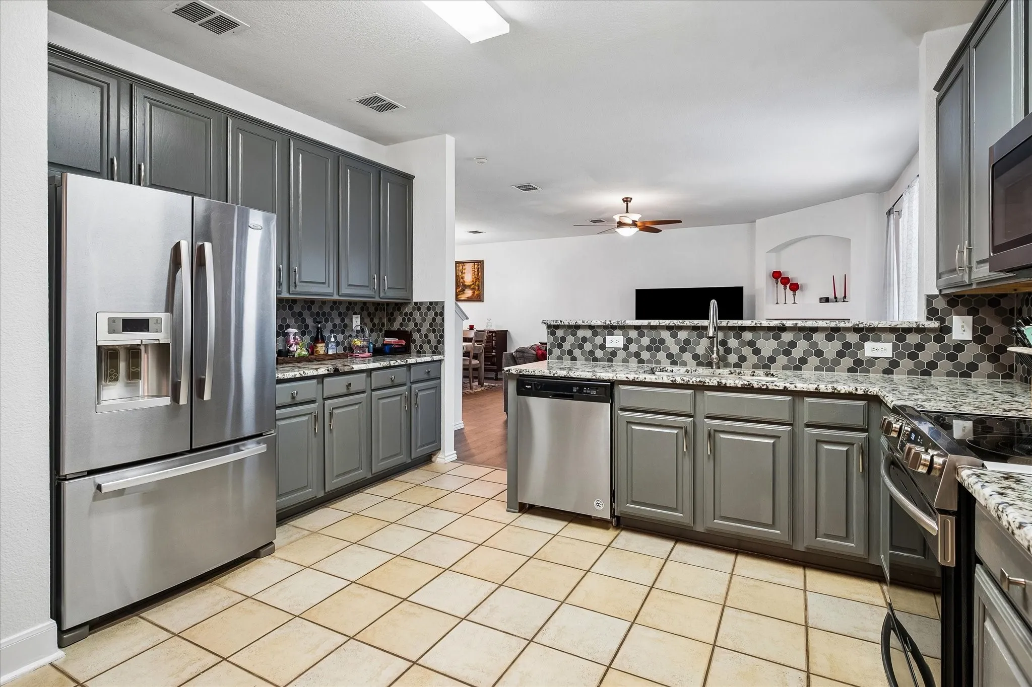 Spacious kitchen featuring gray cabinetry, stainless steel appliances, speckled countertops, a hexagon tile backsplash, and ceramic tile flooring